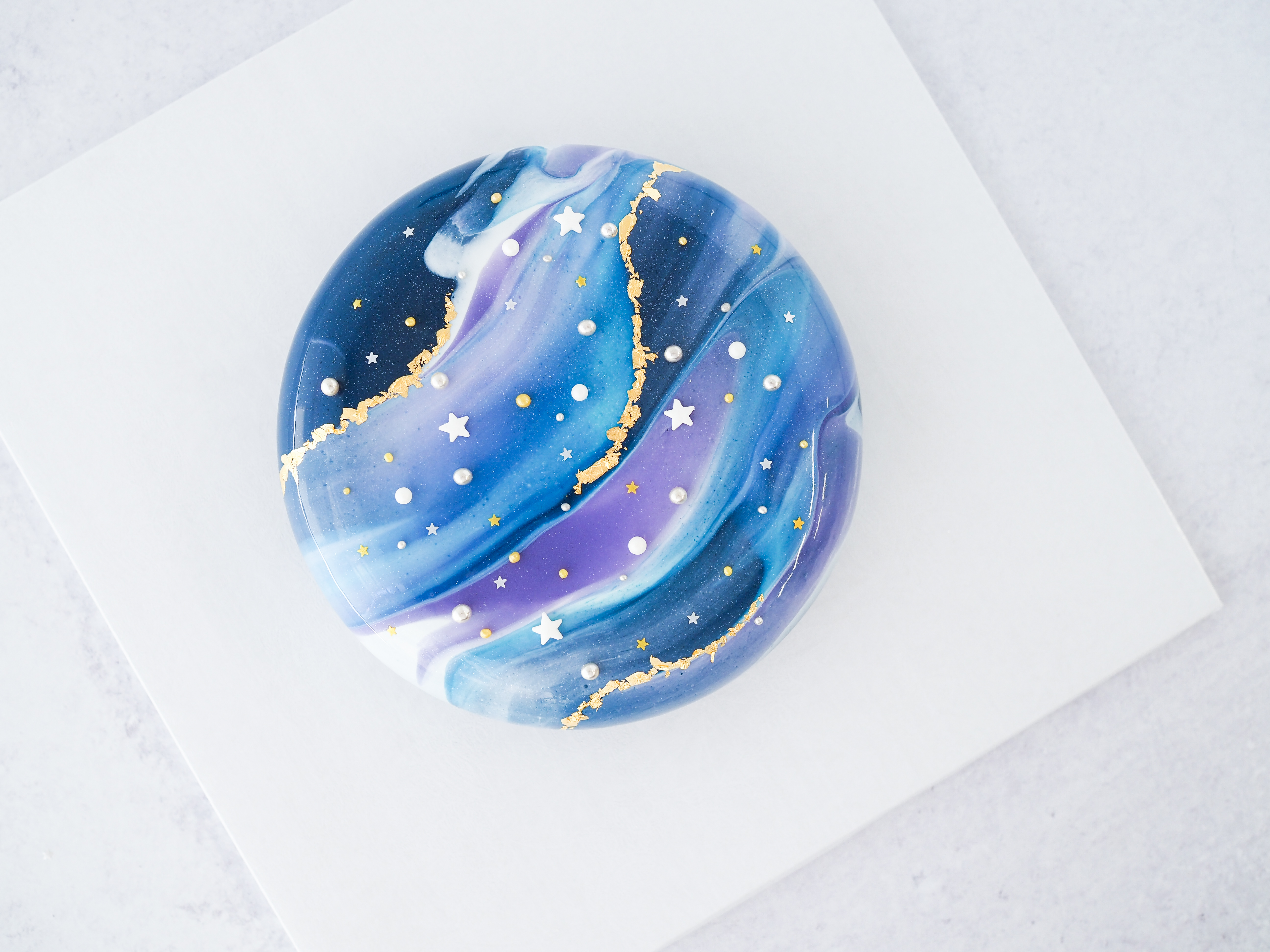 A galaxy-like circular cake glazed with swirls of purple and blues, and showered with star candies.