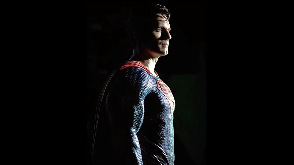 Henry Cavill as Superman standing in the iconic blue and red suit standing in a black void with dramatic lighting illuminating the side of his face