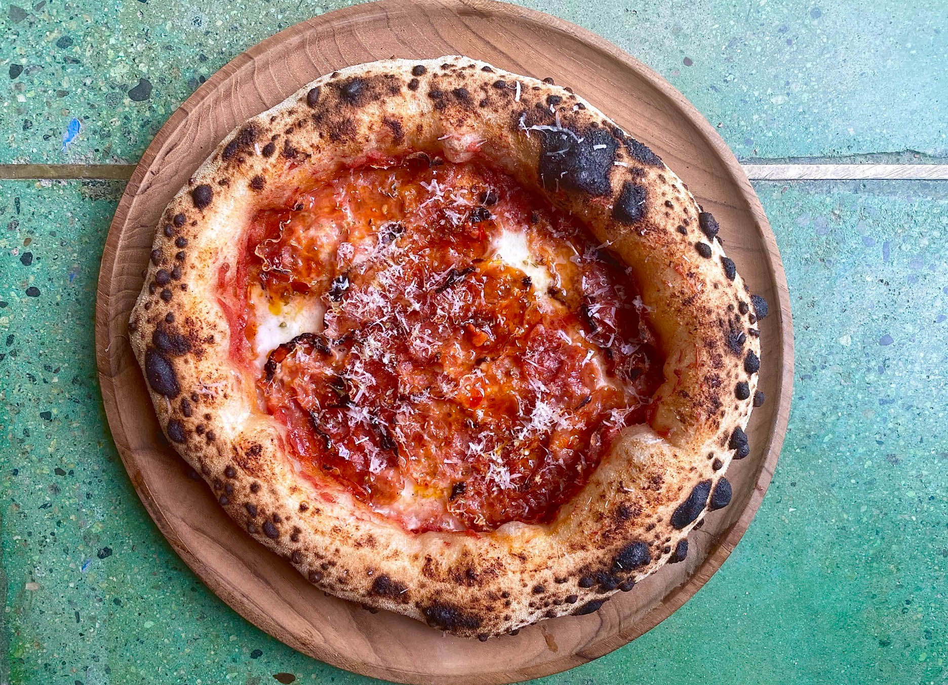 An overhead shot of a puffy crust small pizza on a teal colored marble floor.