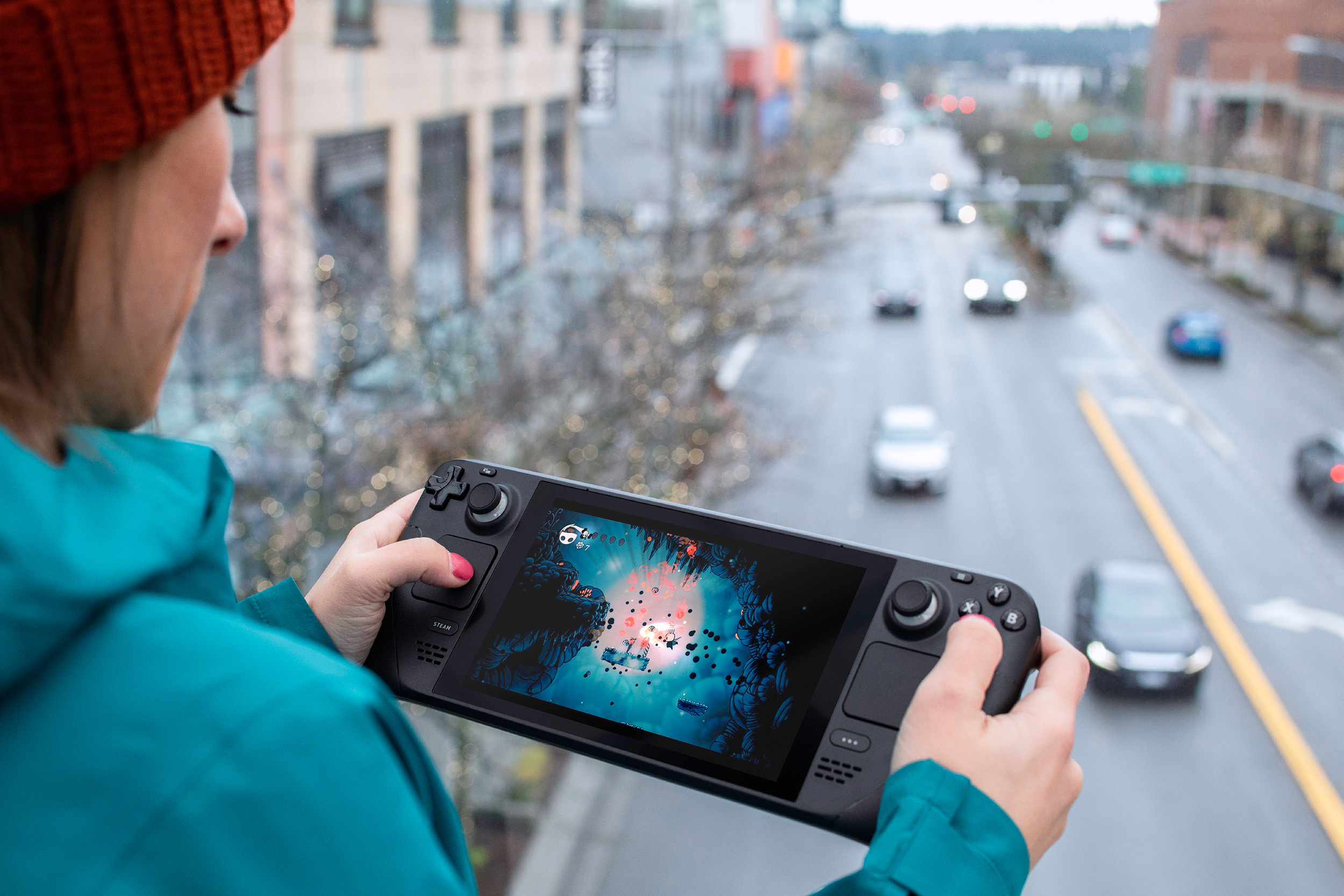 A woman playing Hollow Knight on the Steam Deck. In the background, cars drive down a street.