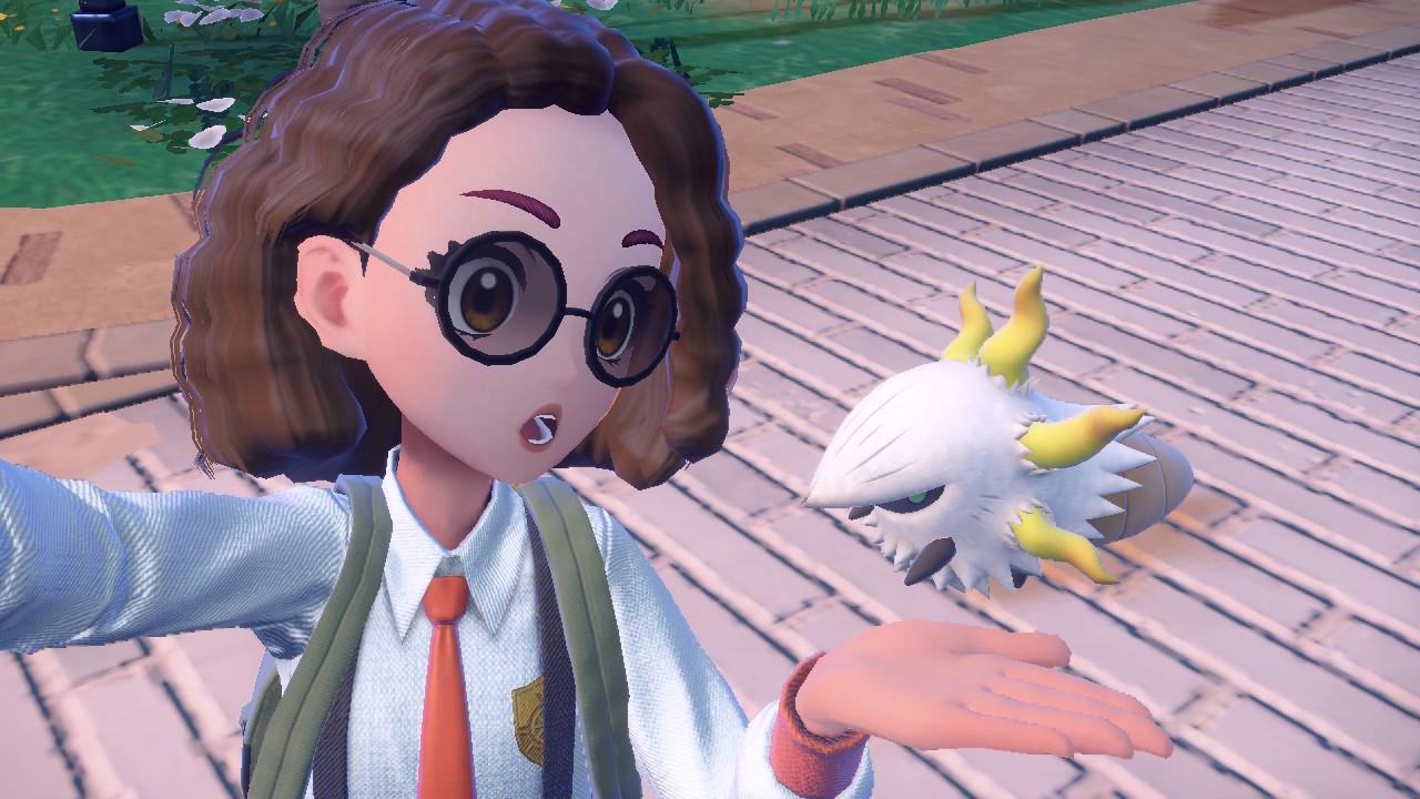 An image of a shiny Larvesta in Pokémon Scarlet and Violet. Instead of having an orangish-red appendages, it has gold ones. The Pokémon trainer is taking a selfie with it and she is holding her hand out to show it off.