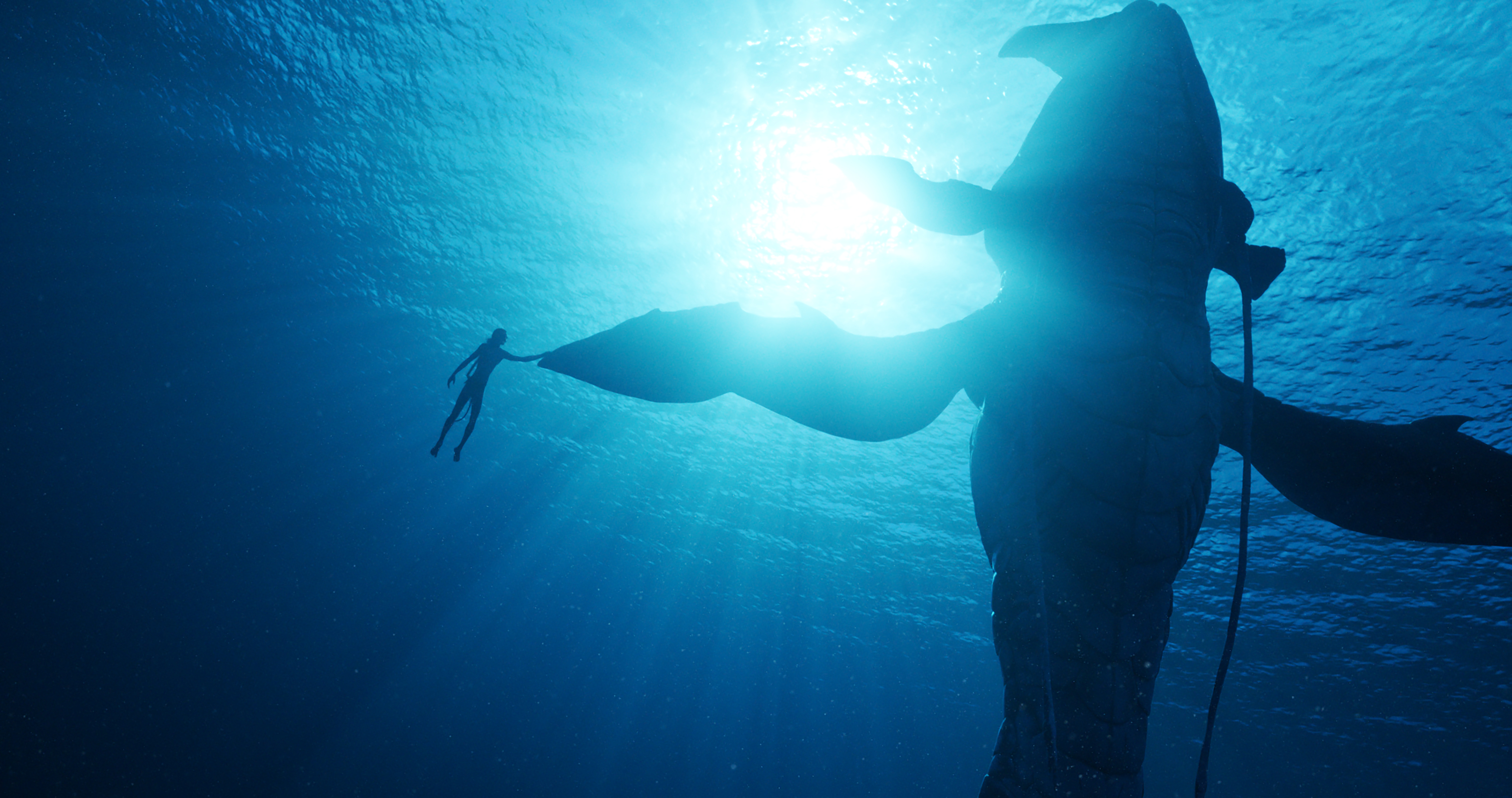A space whale and a Na’vi teenager hold hands/fins underwater in Avatar: The Way of Water.
