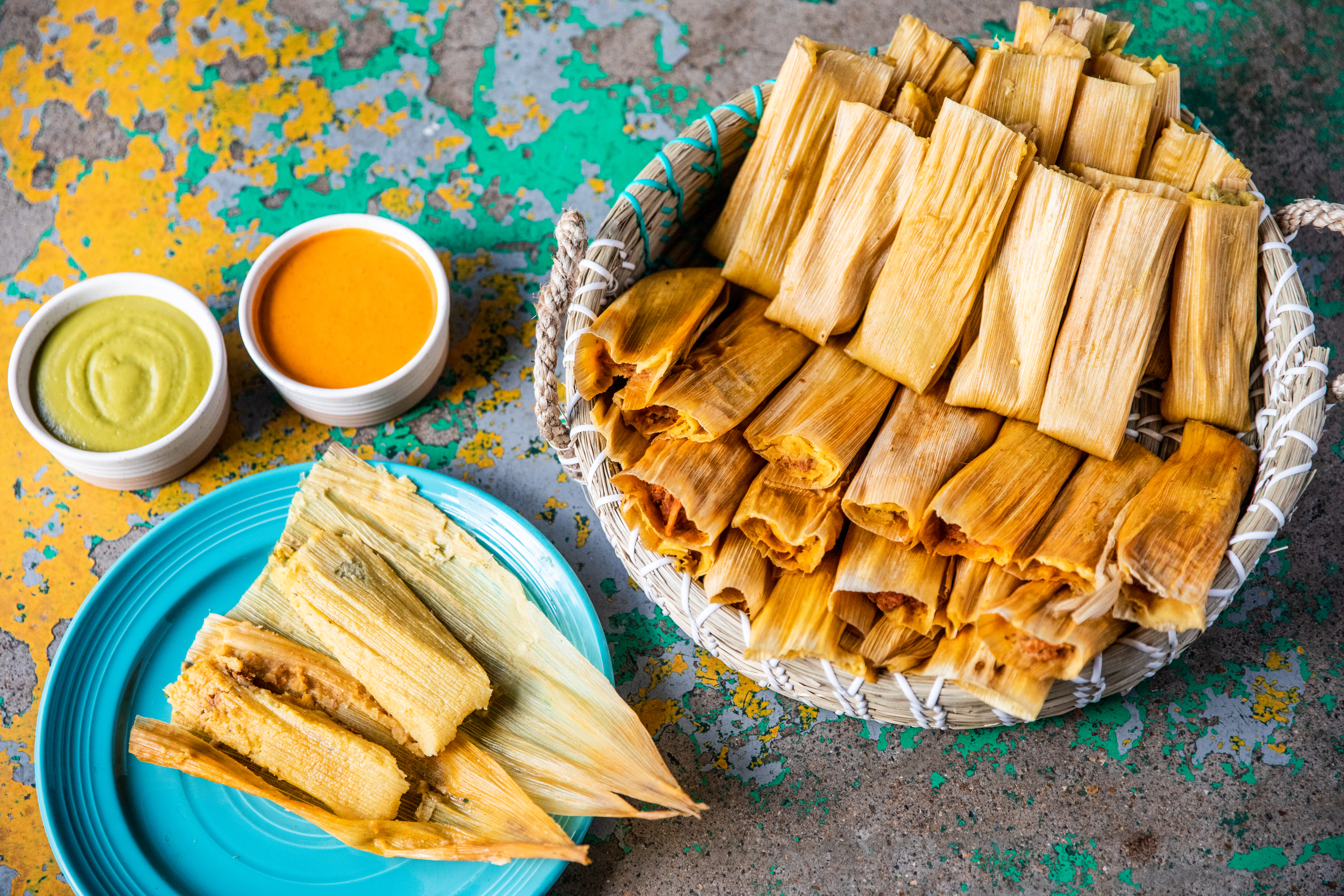A spread of tamales with green and orange salsa.