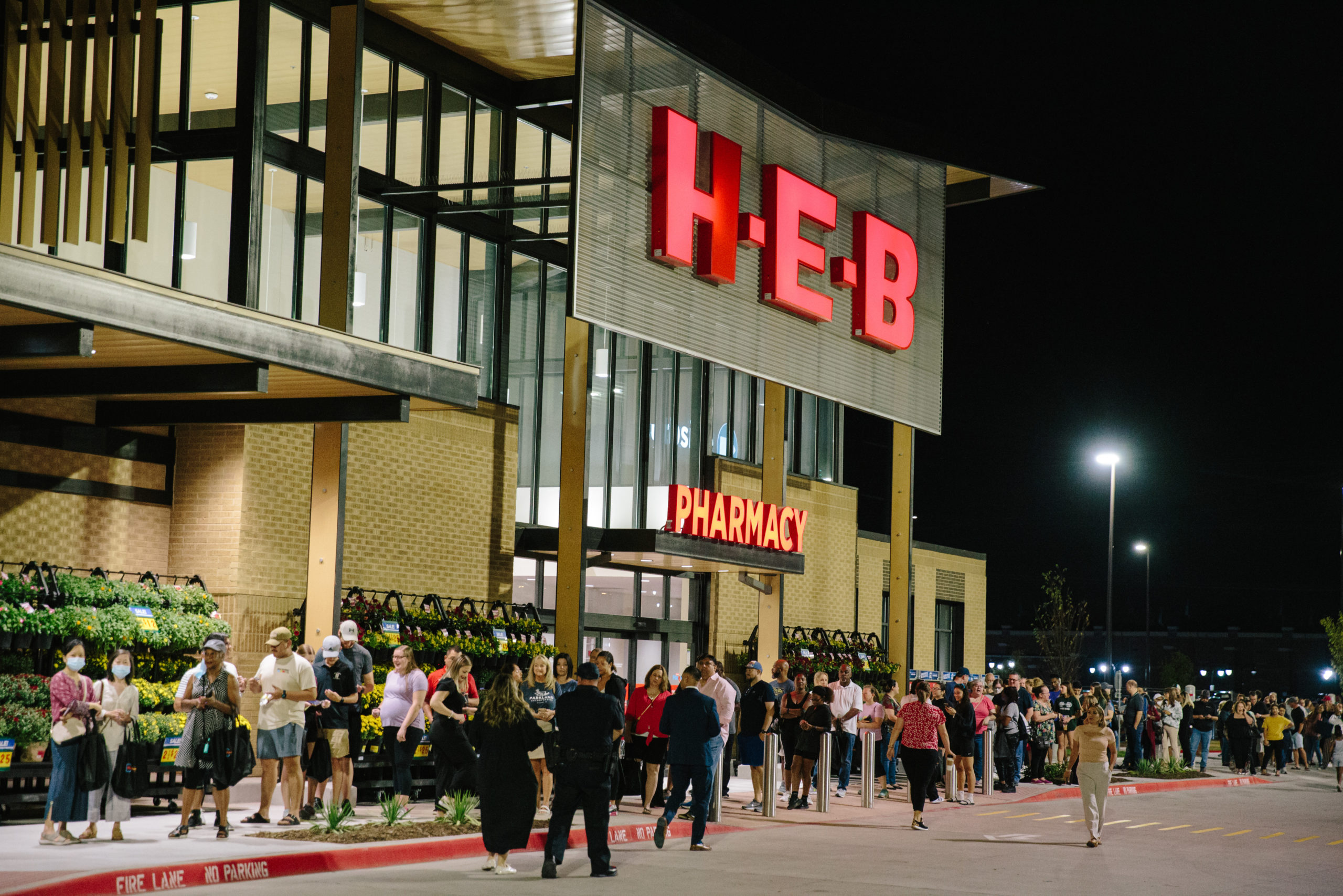 People line up outside the grand opening of an H-E-B grocery store in the evening.