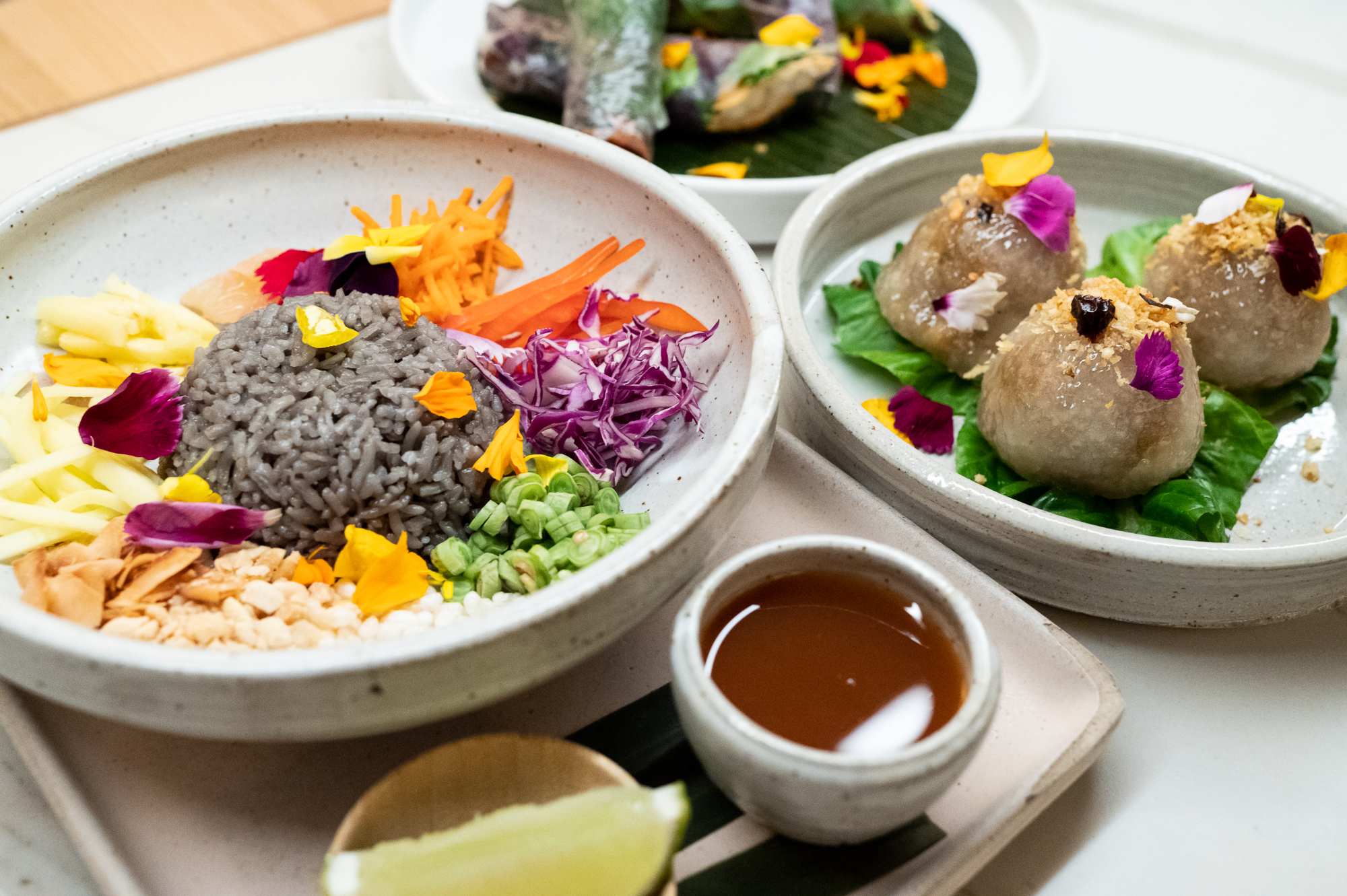 Rainbow rice and sakoo, a type of tapioca dumpling, on plates, with sauce and a lime wedge.
