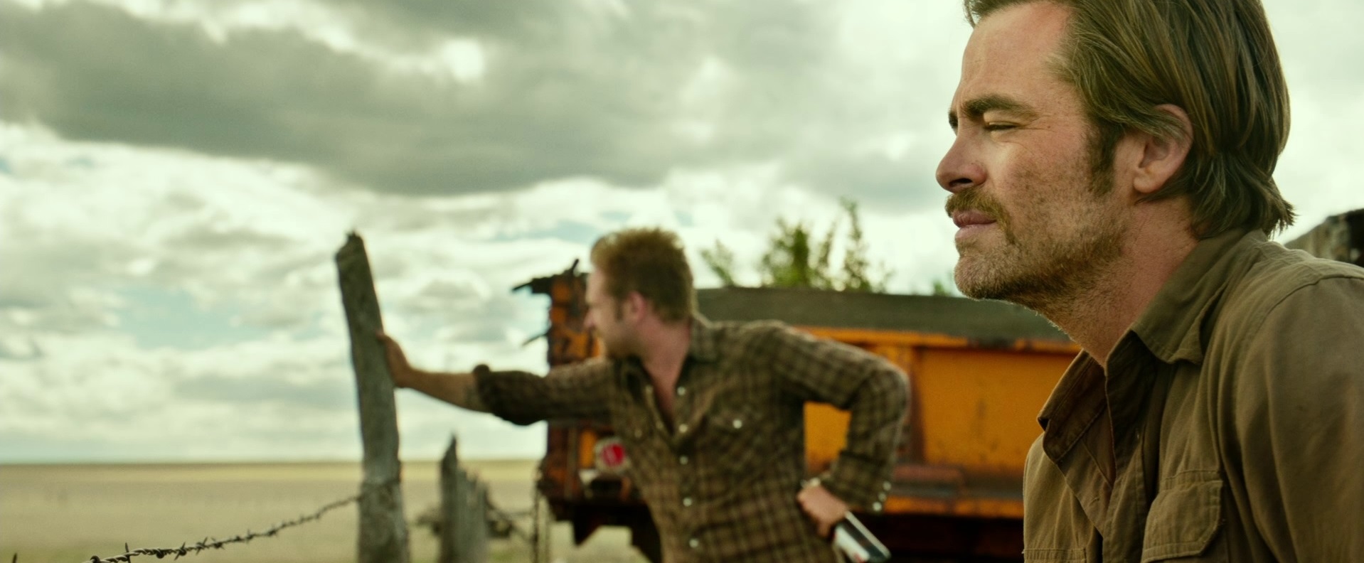 Chris Pine looks pensive as Ben Foster leans against something and looks out into the horizon in Hell or High Water.