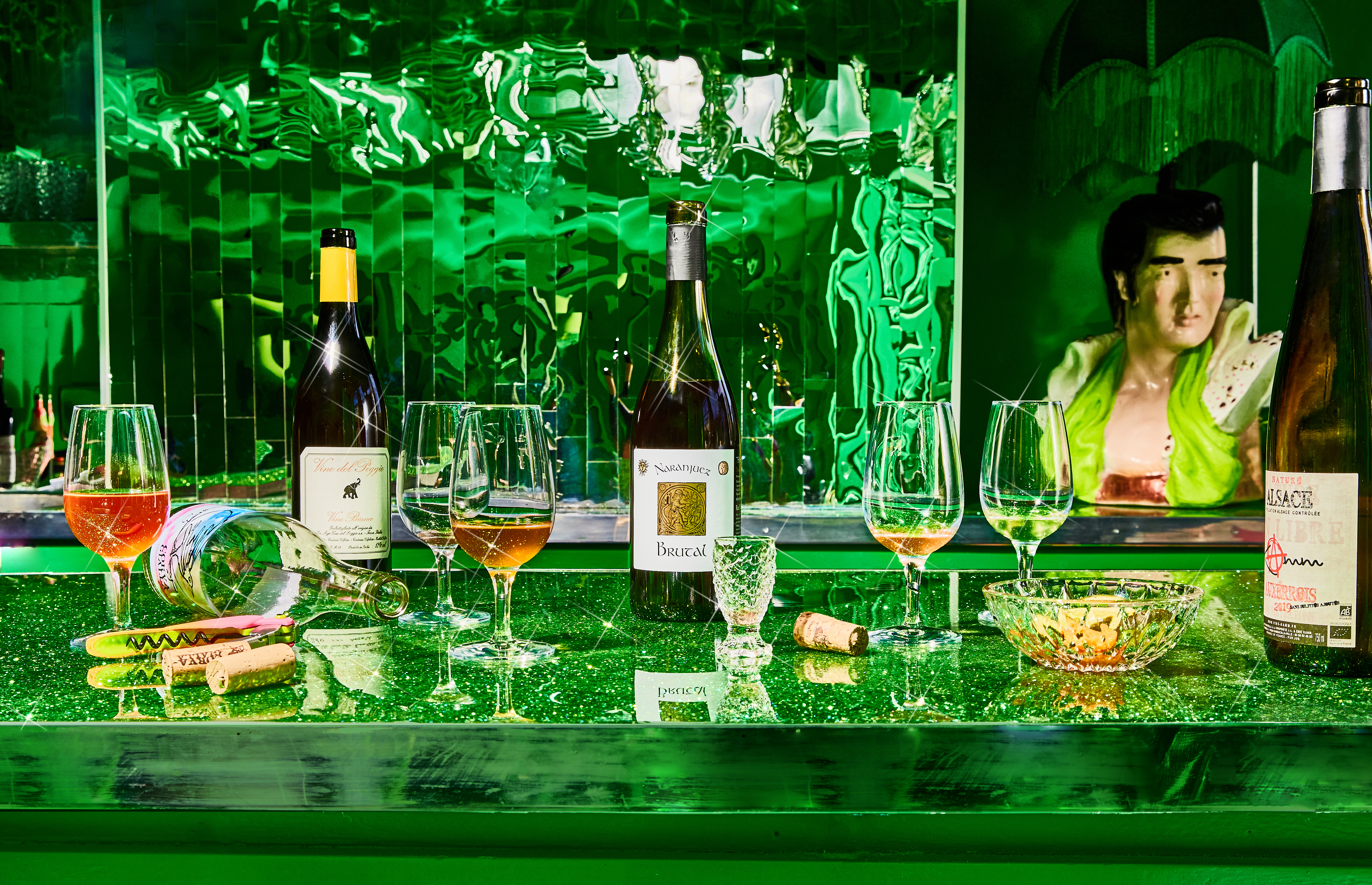 Two bottles of wine and several glasses on top of a glittery green bar.