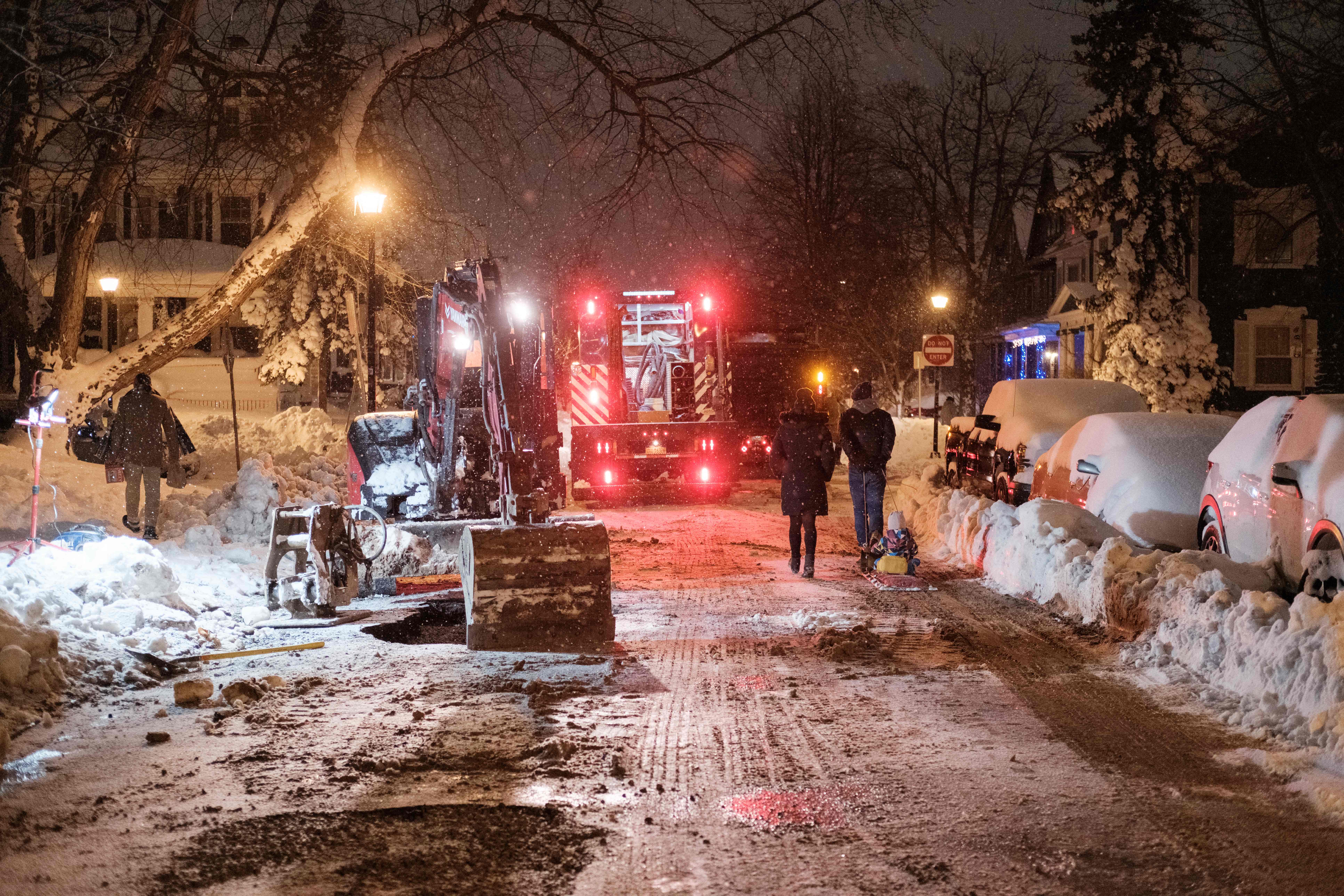Repair vehicles and workers on a snowy street after dark.