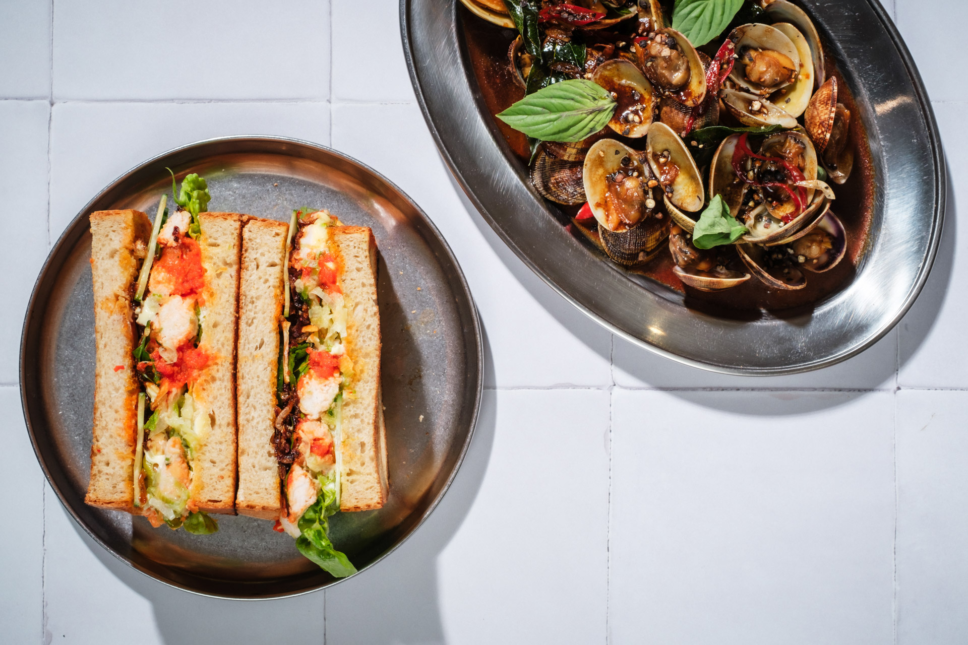 A Hainanese chicken sando and platter of clams, both on silver dishes