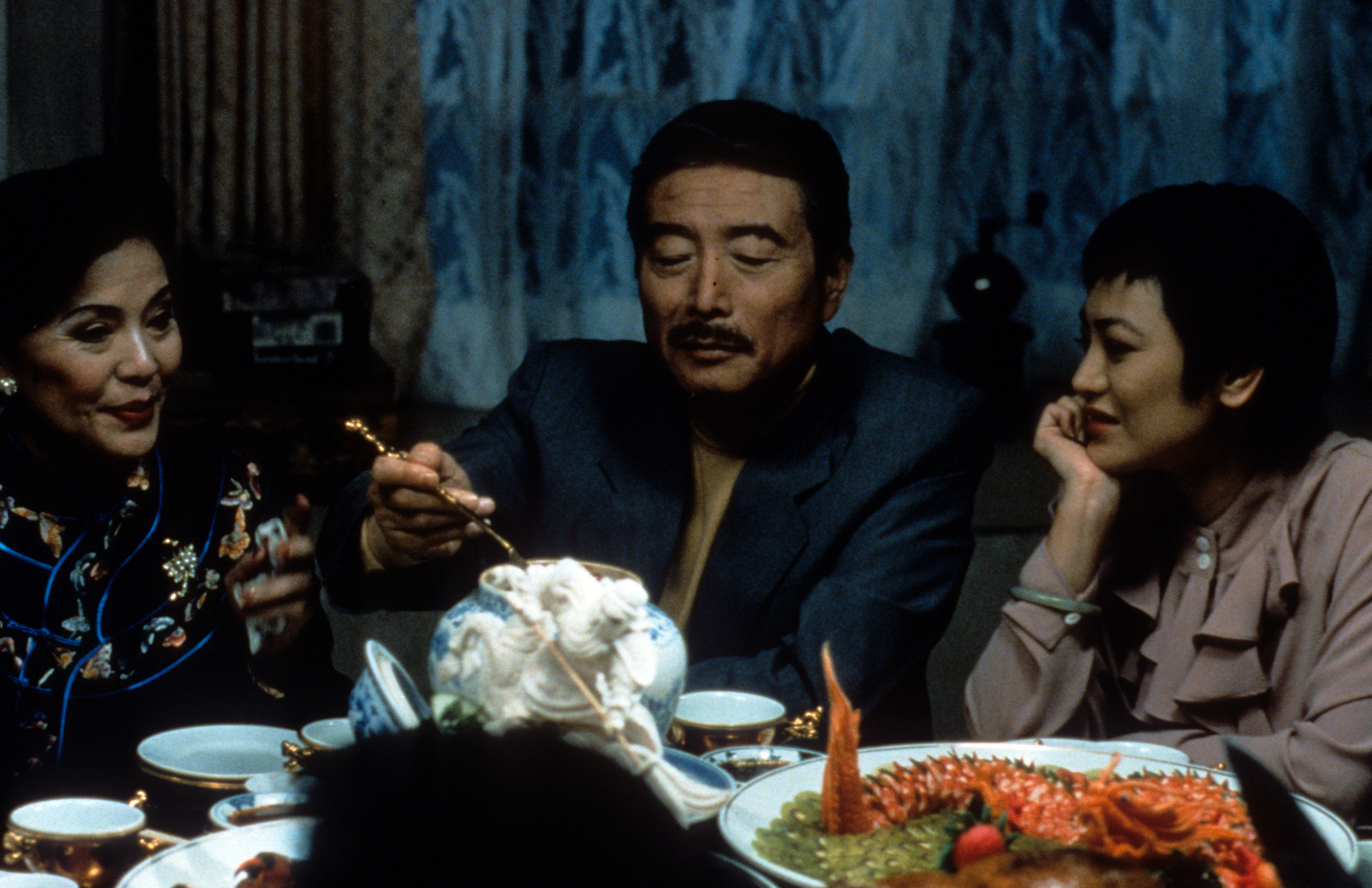 一个男人坐在两个女人中间，用餐具从桌子上拿起食物。