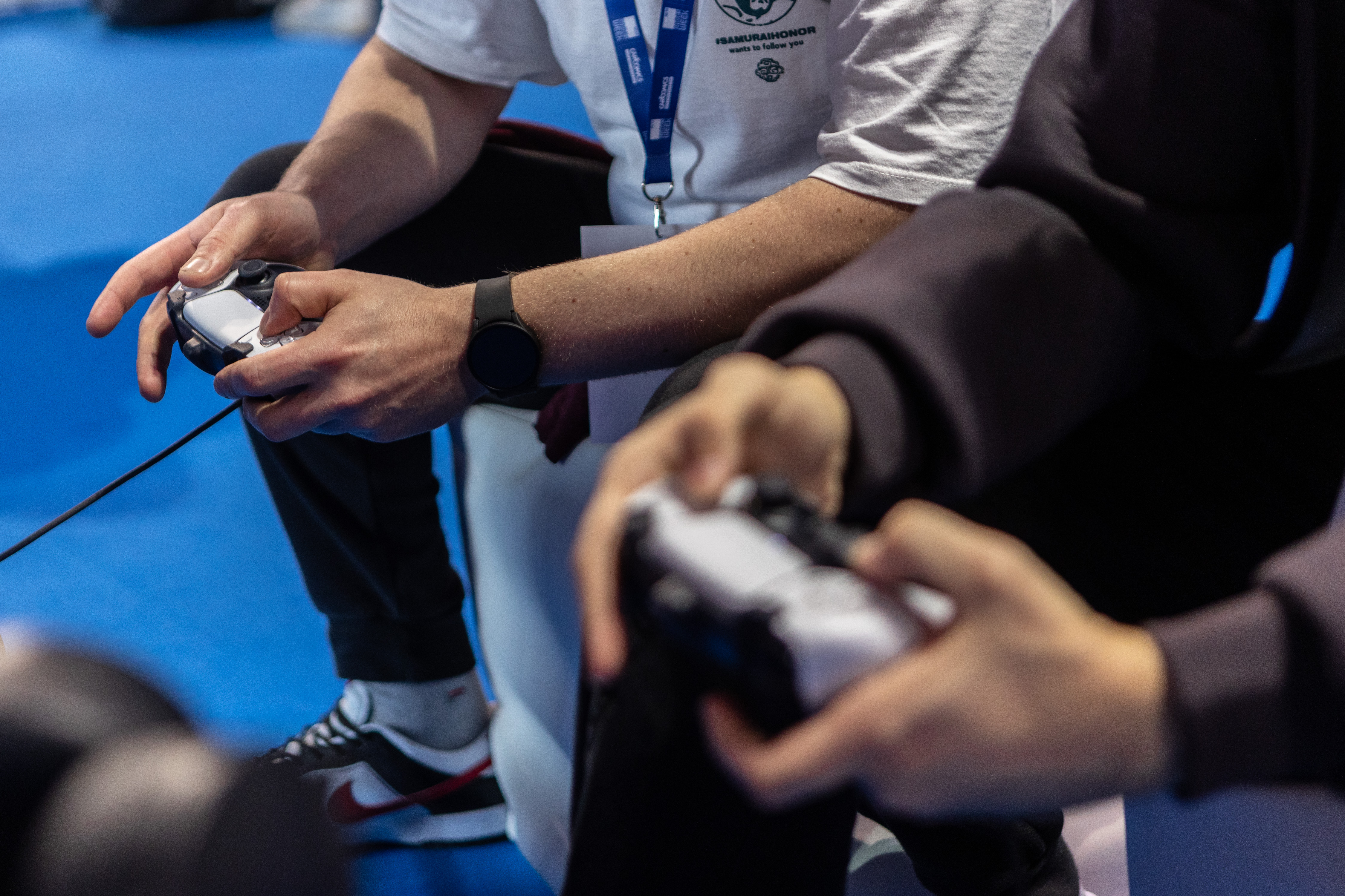 A close-up of two people holding PlayStation 5 controllers at an event.