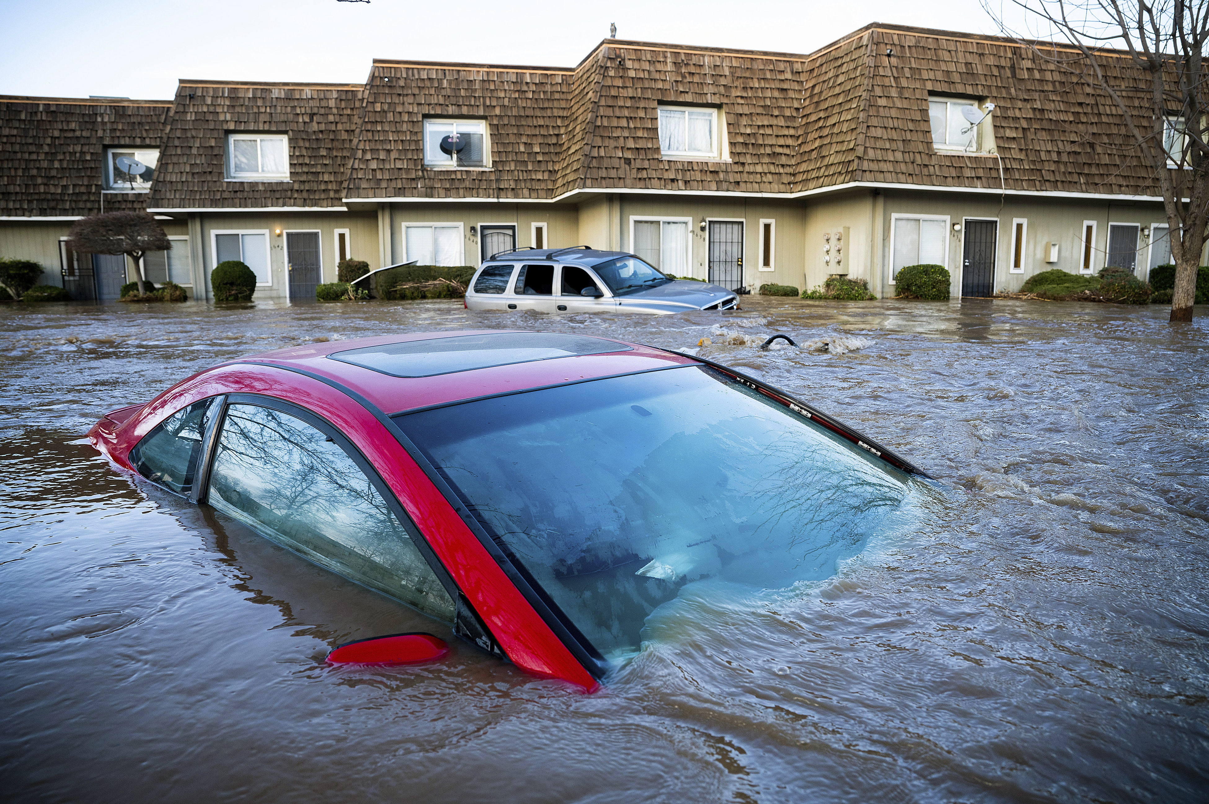 A parked car up to its windows in brown floodwater, with a line of houses behind it.