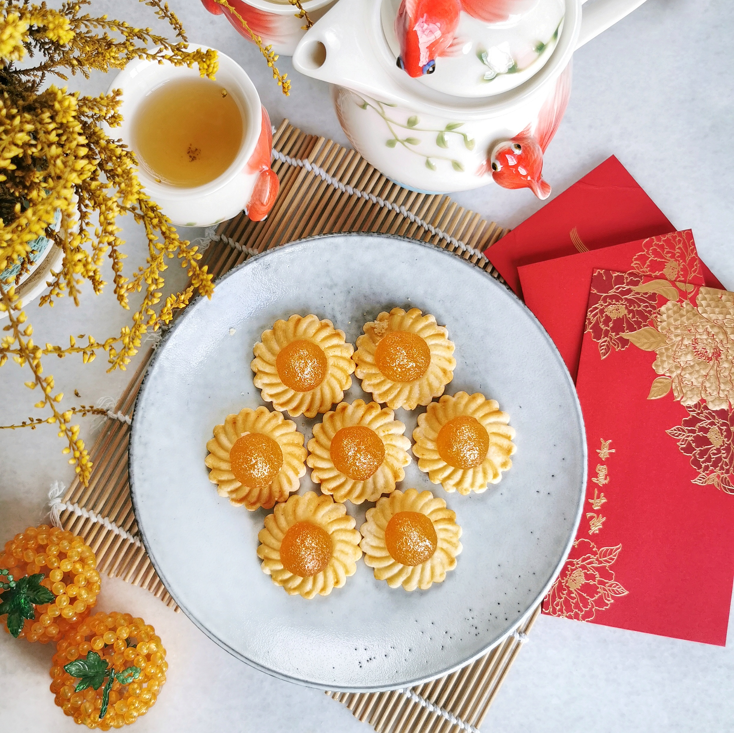 A plate of bite-size tarts is surrounded by tea and red money envelopes.