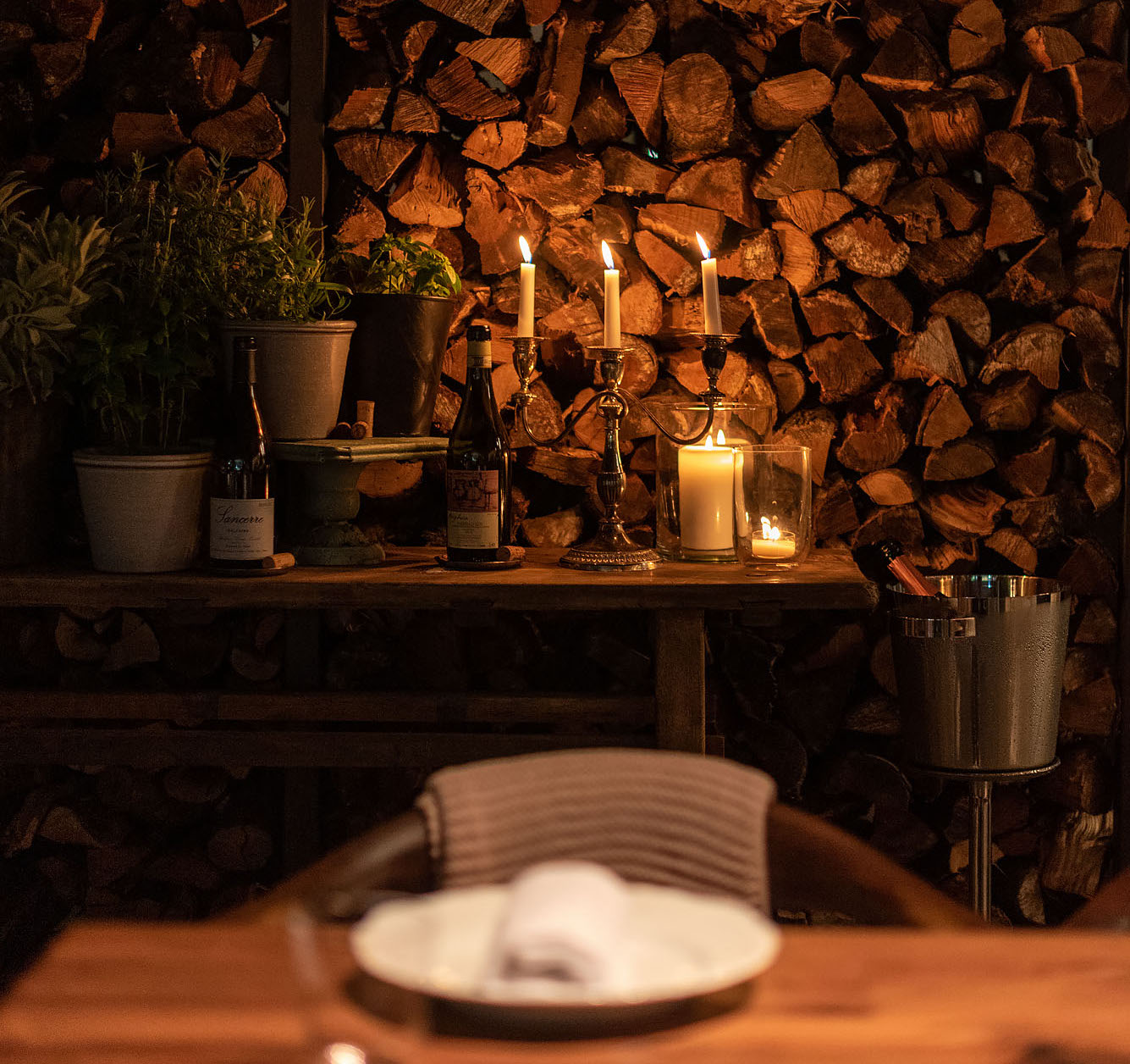 Three lit candles against a backdrop of stone and wood in a moody, dim restaurant.