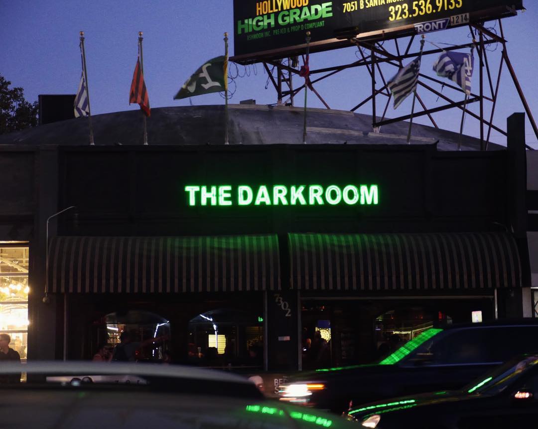 As sun sets, green neon lights the way to a dim dive bar.