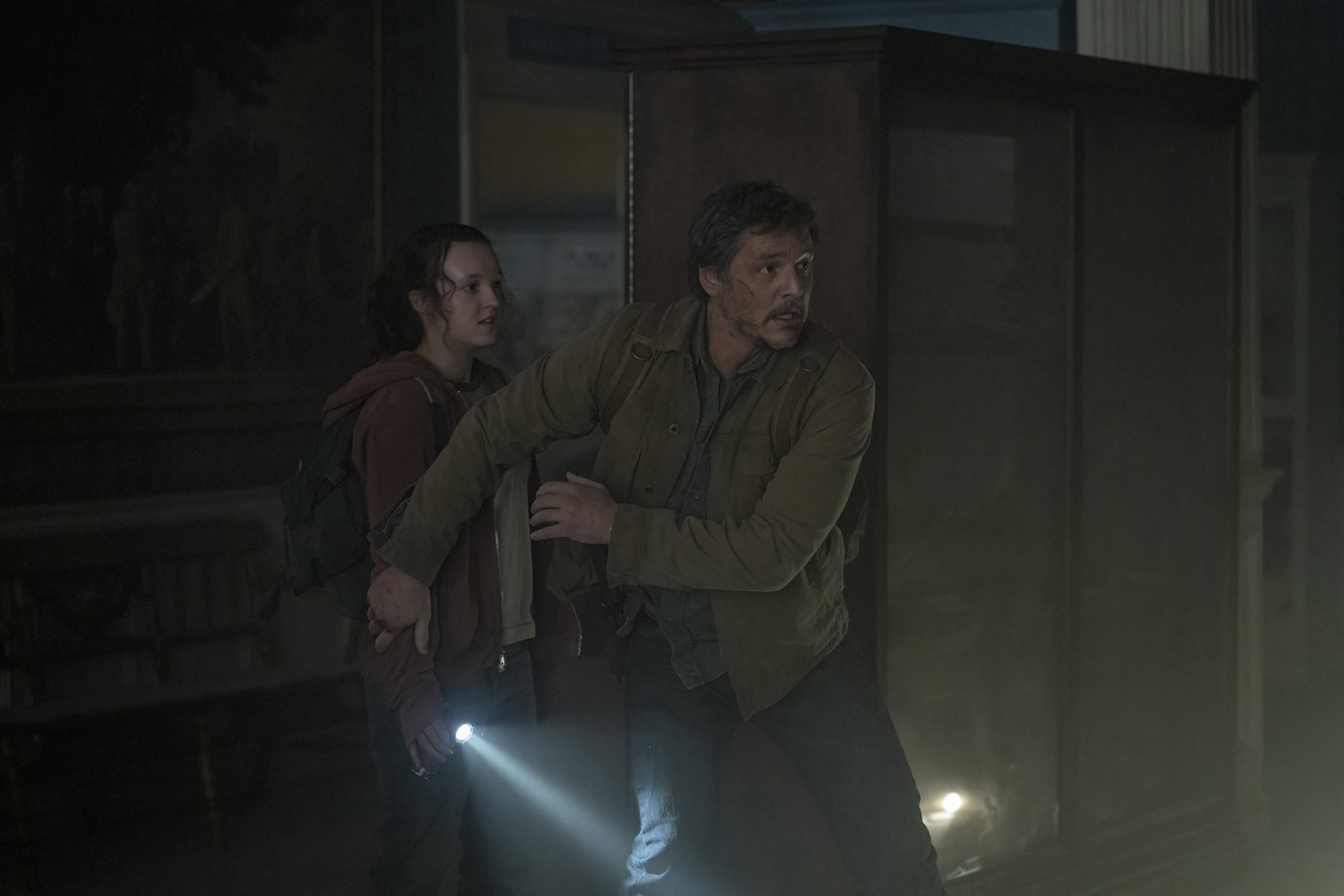 Joel (Pedro Pascal) reaching back to cover Ellie (Bella Ramsey)