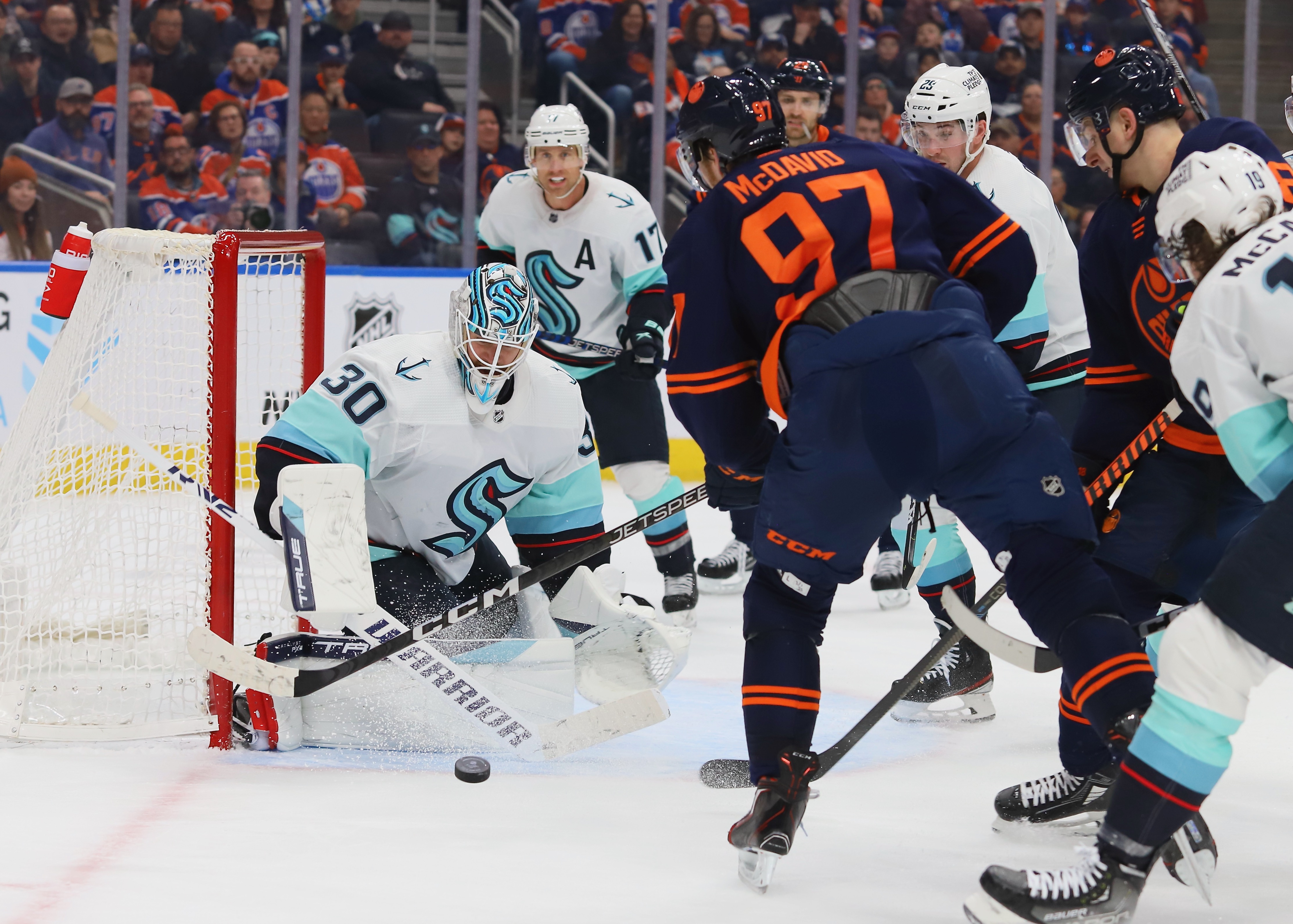Martin Jones stops a shot against Connor McDavid. Jones is angled facing toward the camera, in a Kraken white away jersey, and McDavid has his back to the camera, in the Oilers’ navy alternate jersey