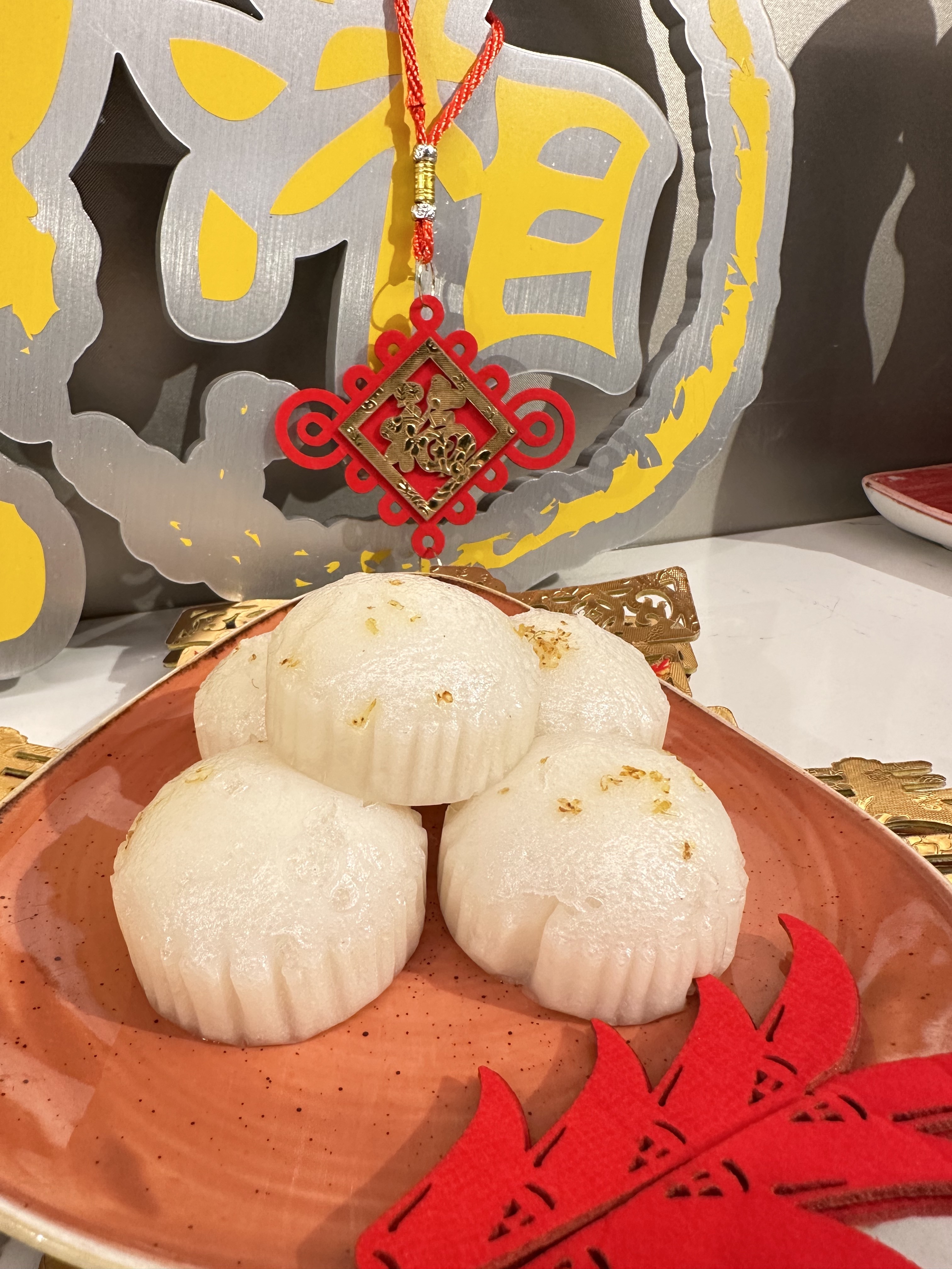A platter of five white rice cakes on a wooden plate with red decorations placed around the plate.