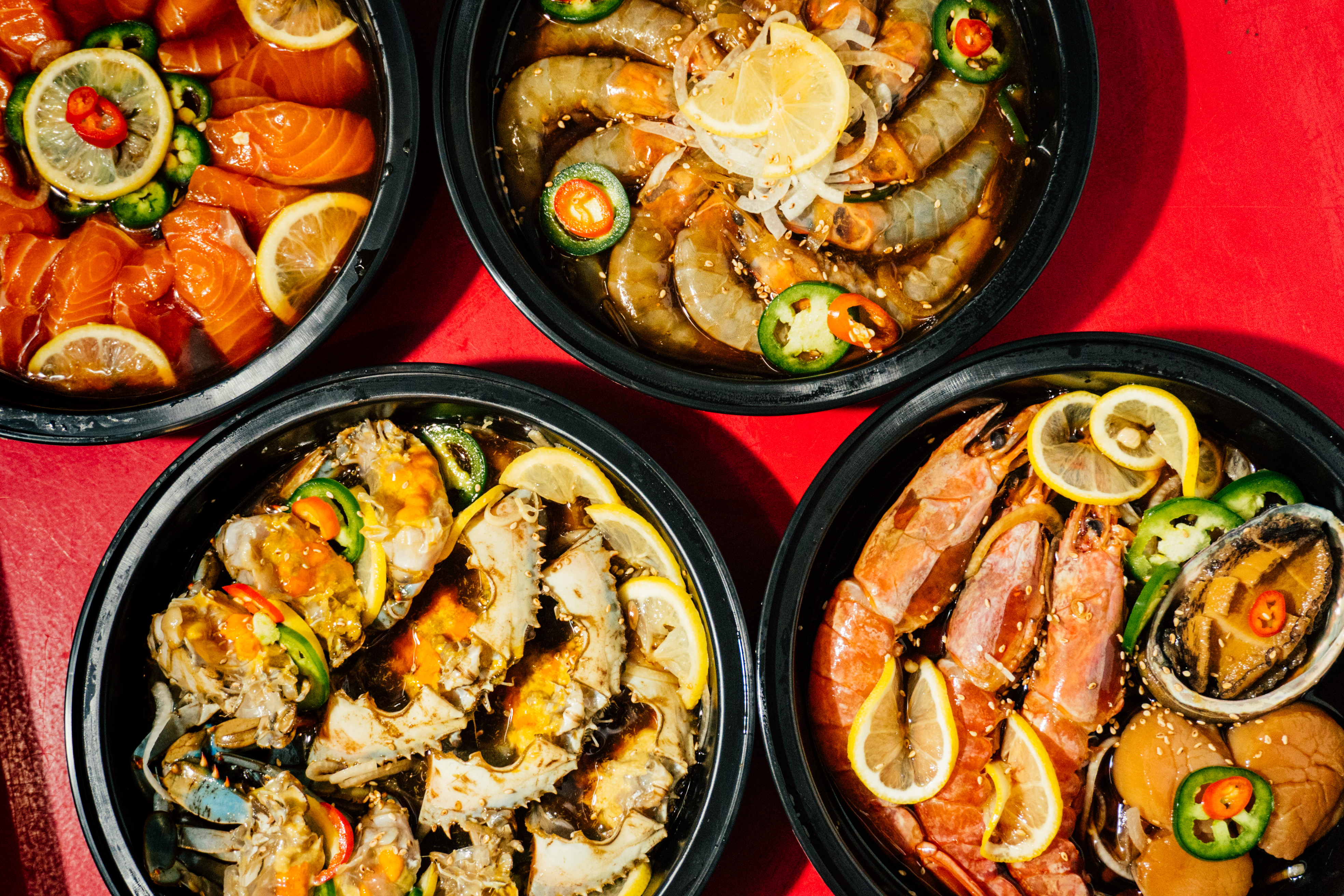A selection of seafood dishes in plastic containers on a red backdrop.