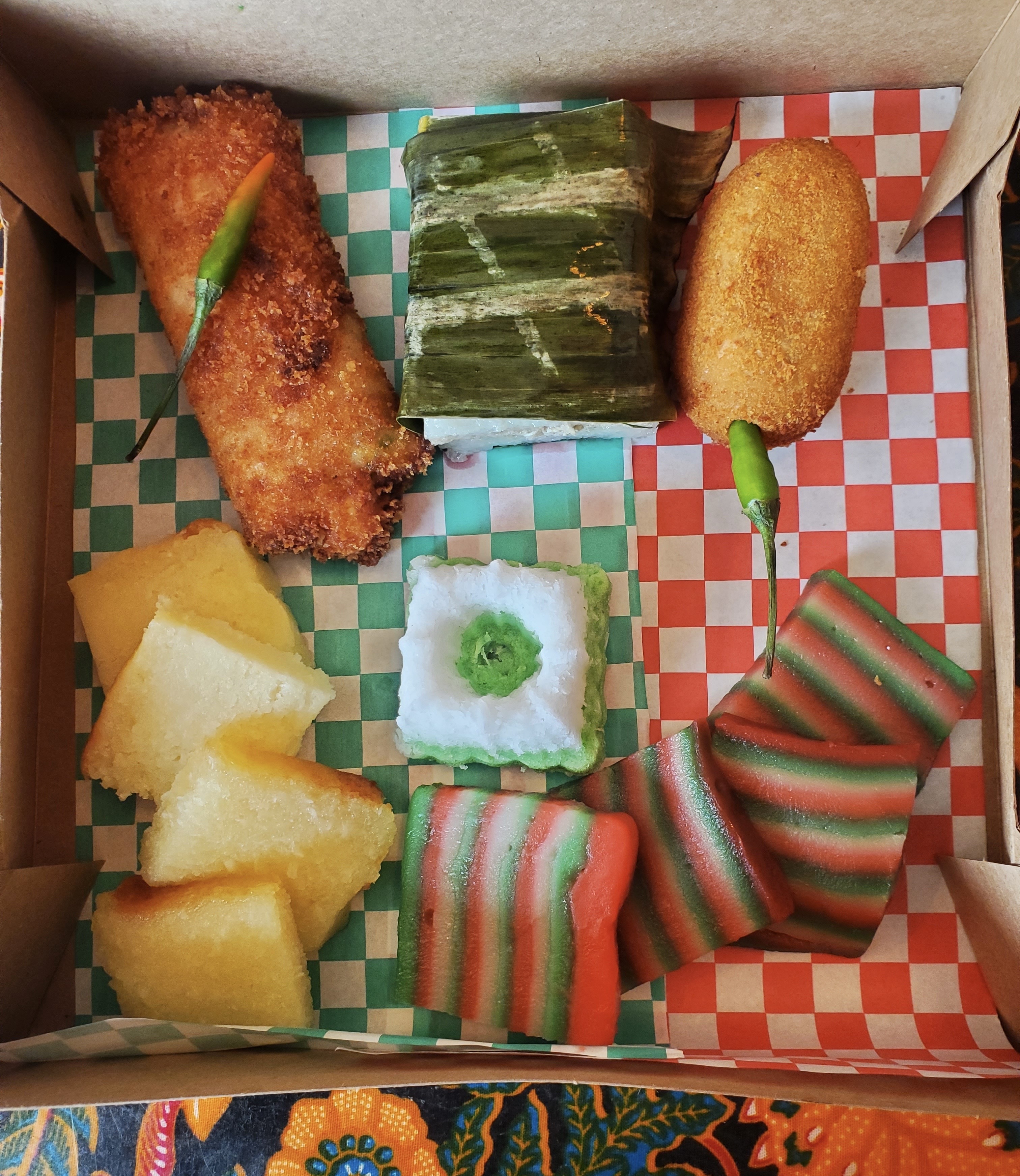 A box lined with green- and red-checkered paper contains an assortment of Indonesian snacks.