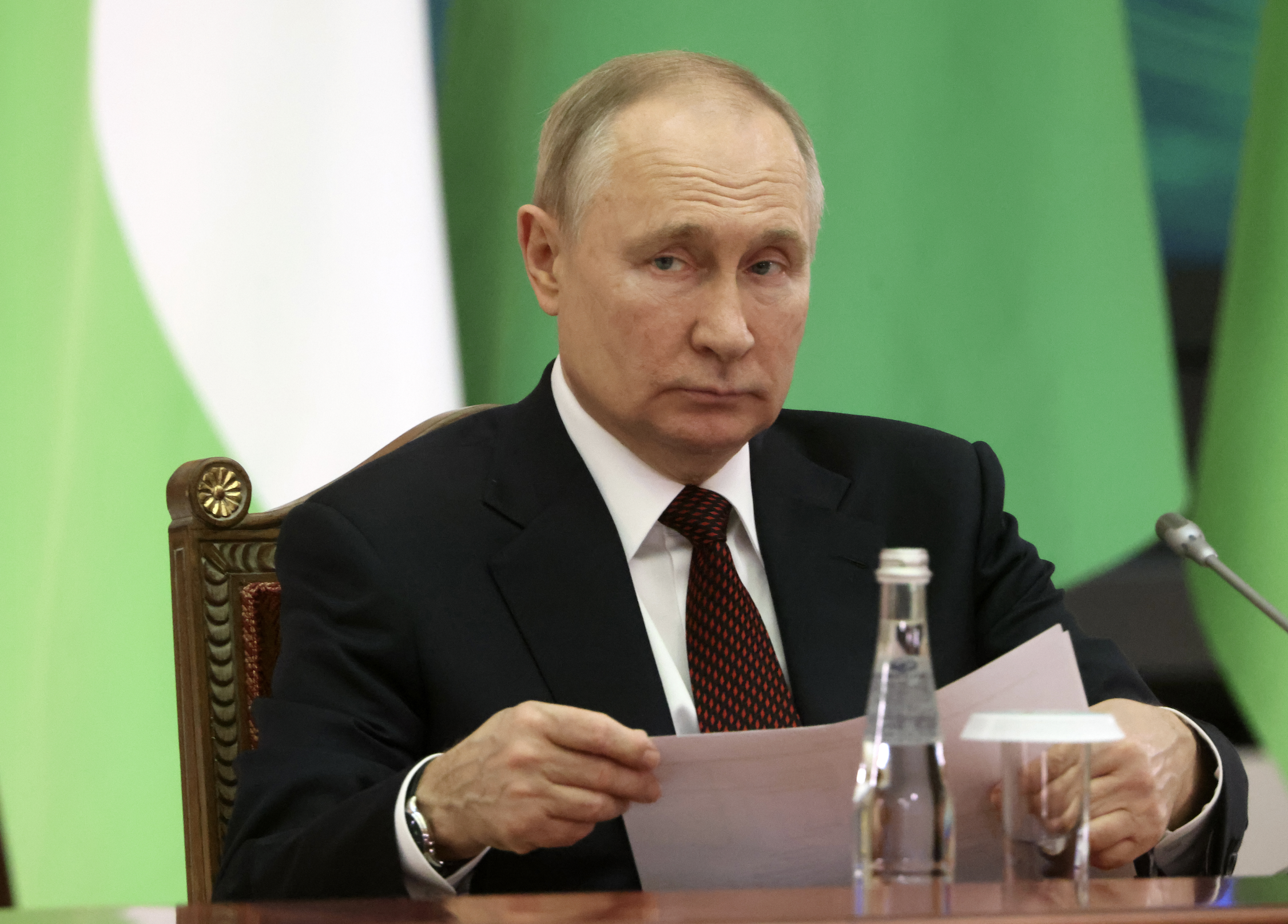 Russian President Vladimir Putin sitting at a table holding papers and not smiling.