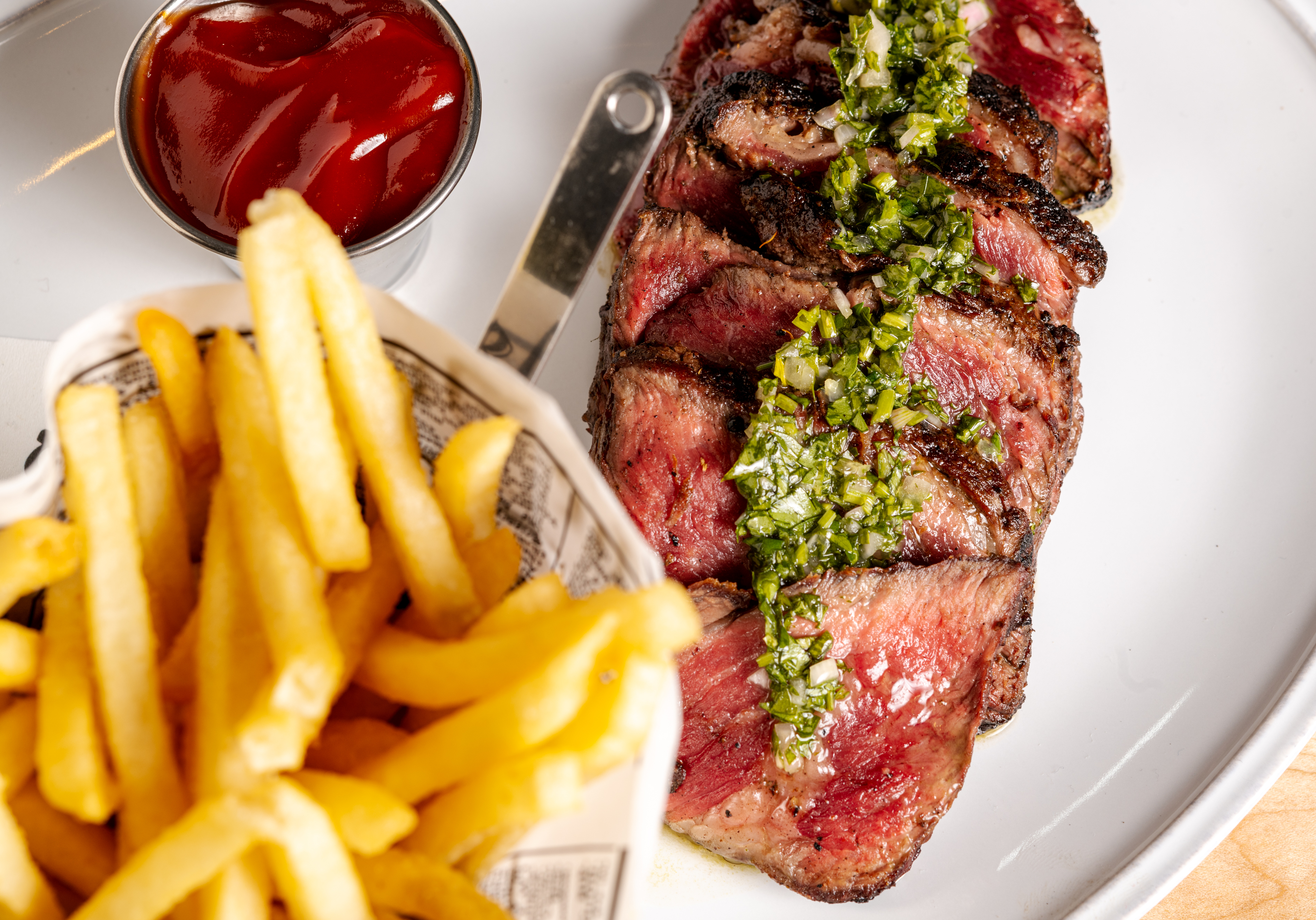 A strip steak sliced up with fries and ketchup to dip.