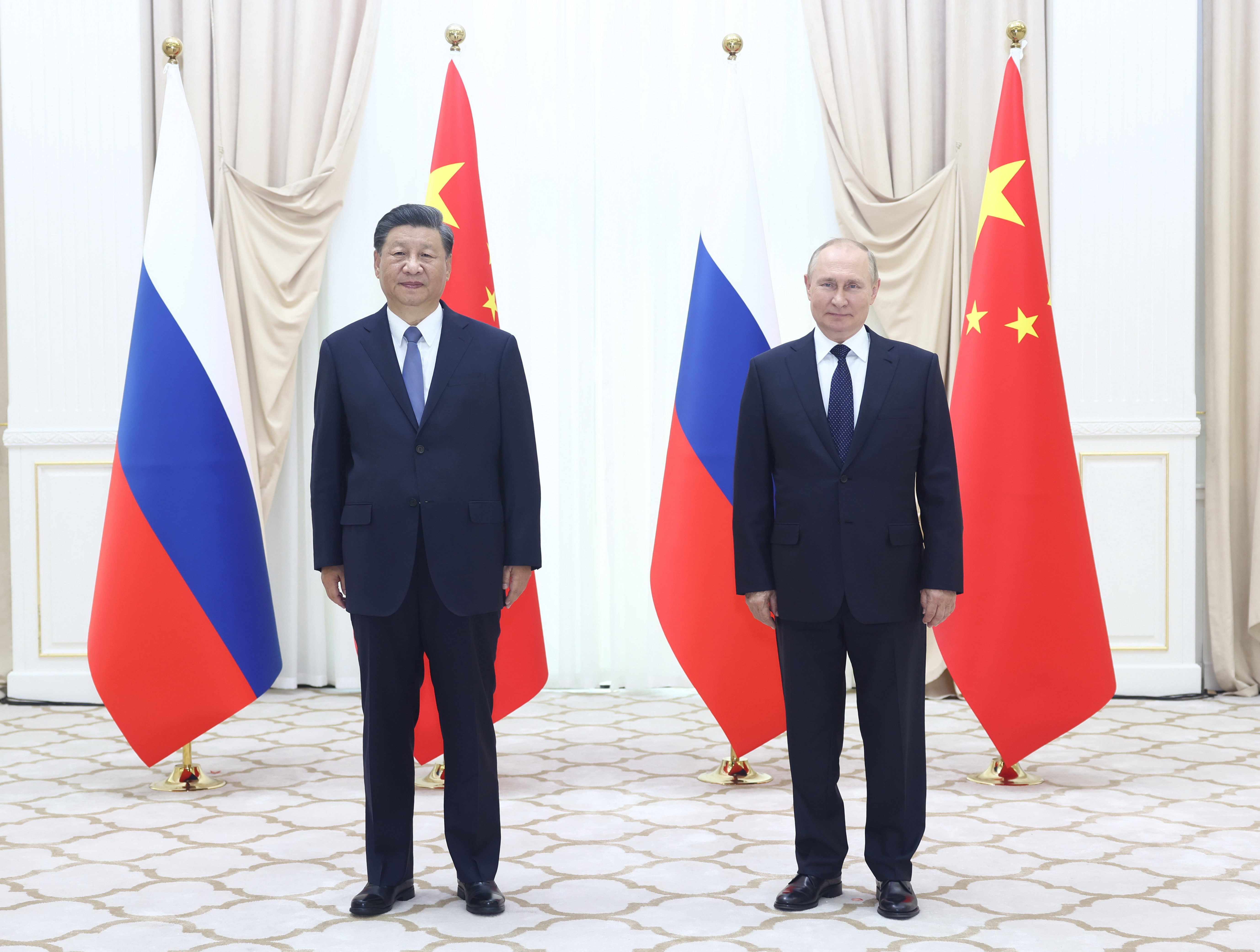 Xi Jinping and Vladimir Putin stand in front of their countries’ flags. 