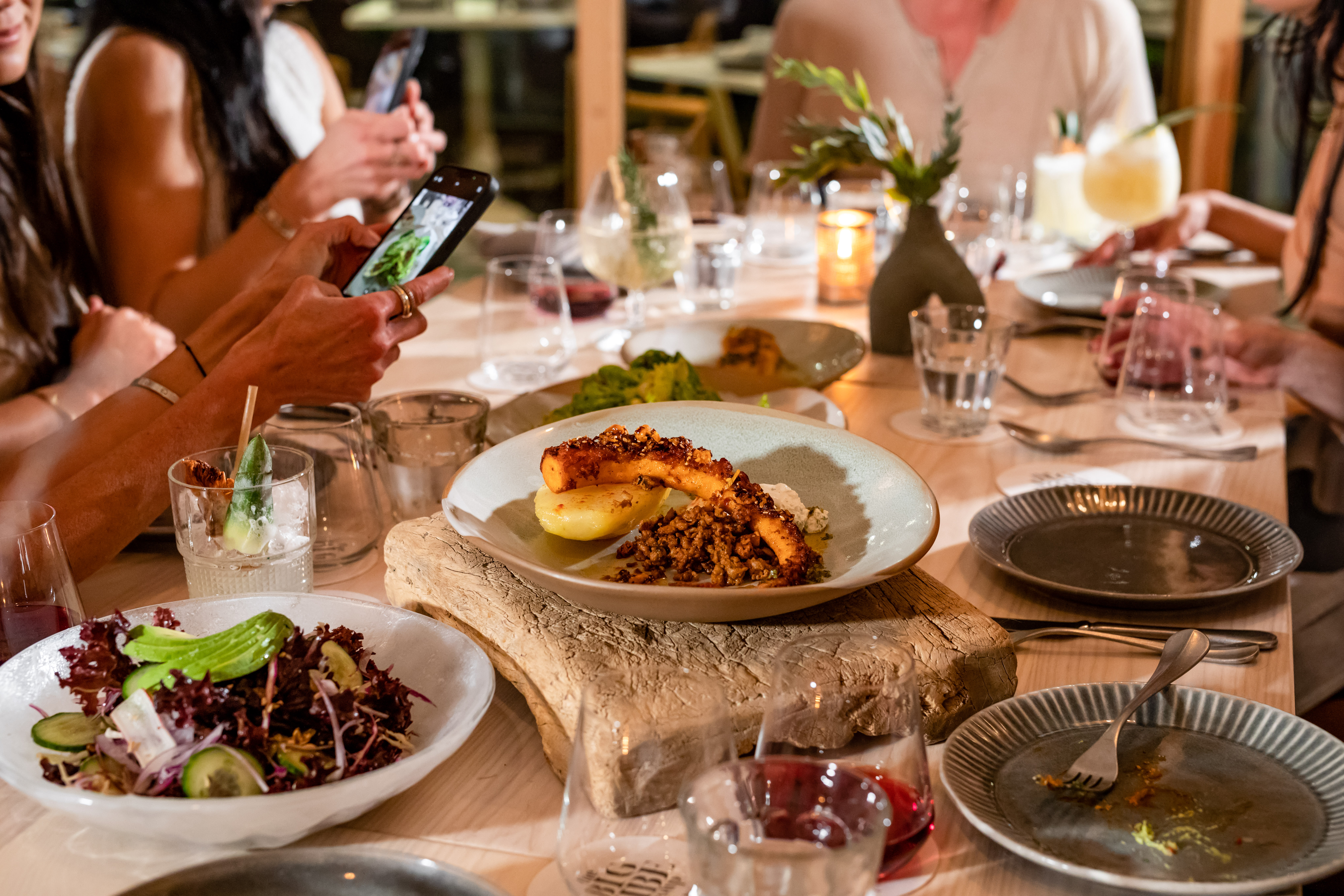 A festive table scape with a plate of octopus in the center, and guests holding their phones to snap a photo.