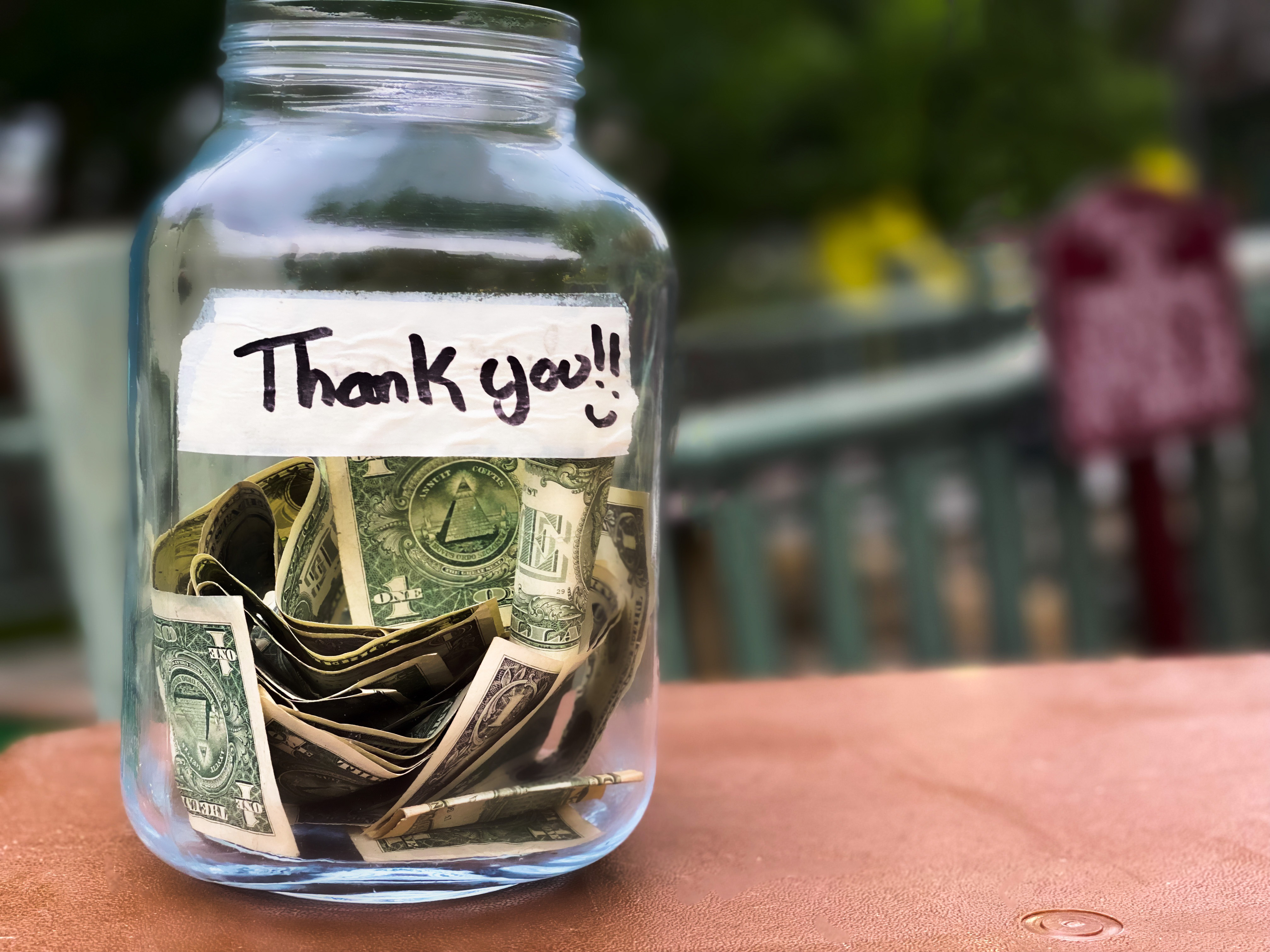 A jar of tips with a piece of tape with thank you written on it sitting on a pink countertop.