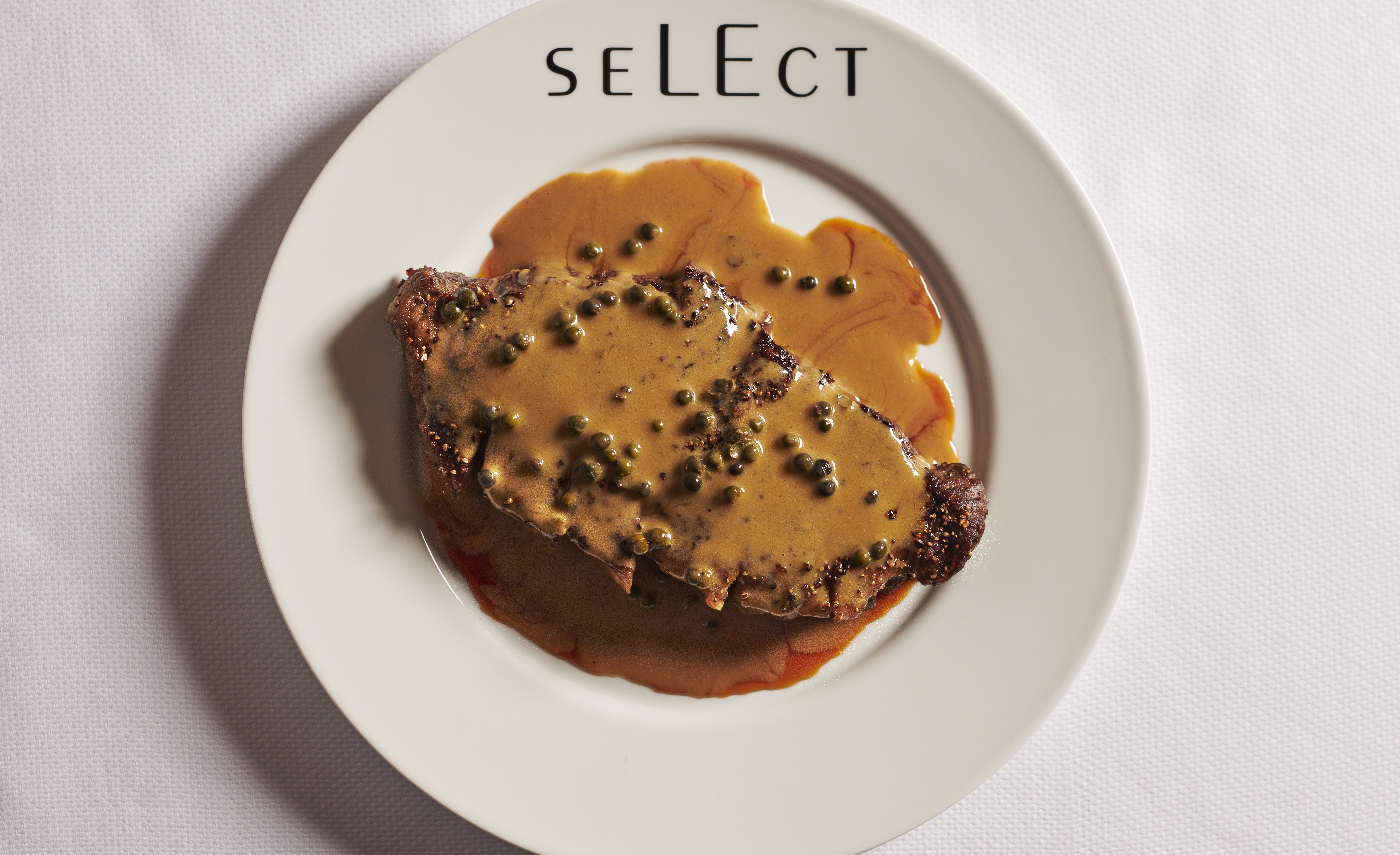 A steak smothered with sauce and peppercorns.