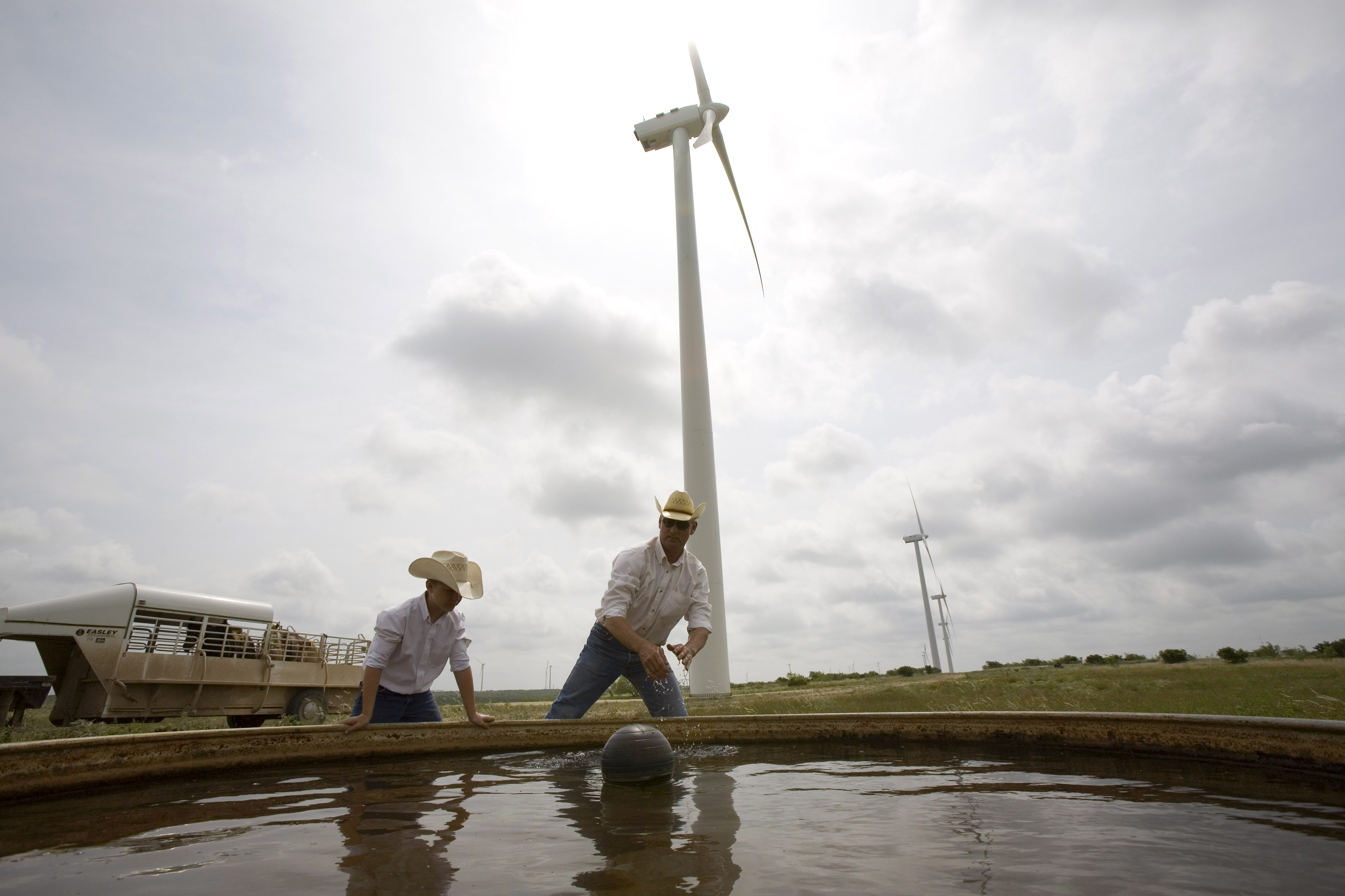 A cattle rancher and his son clean a water tank for their 300 head of cattle on the Lone Star Wind Farm near Abilene, Texas, on June 9, 2007.