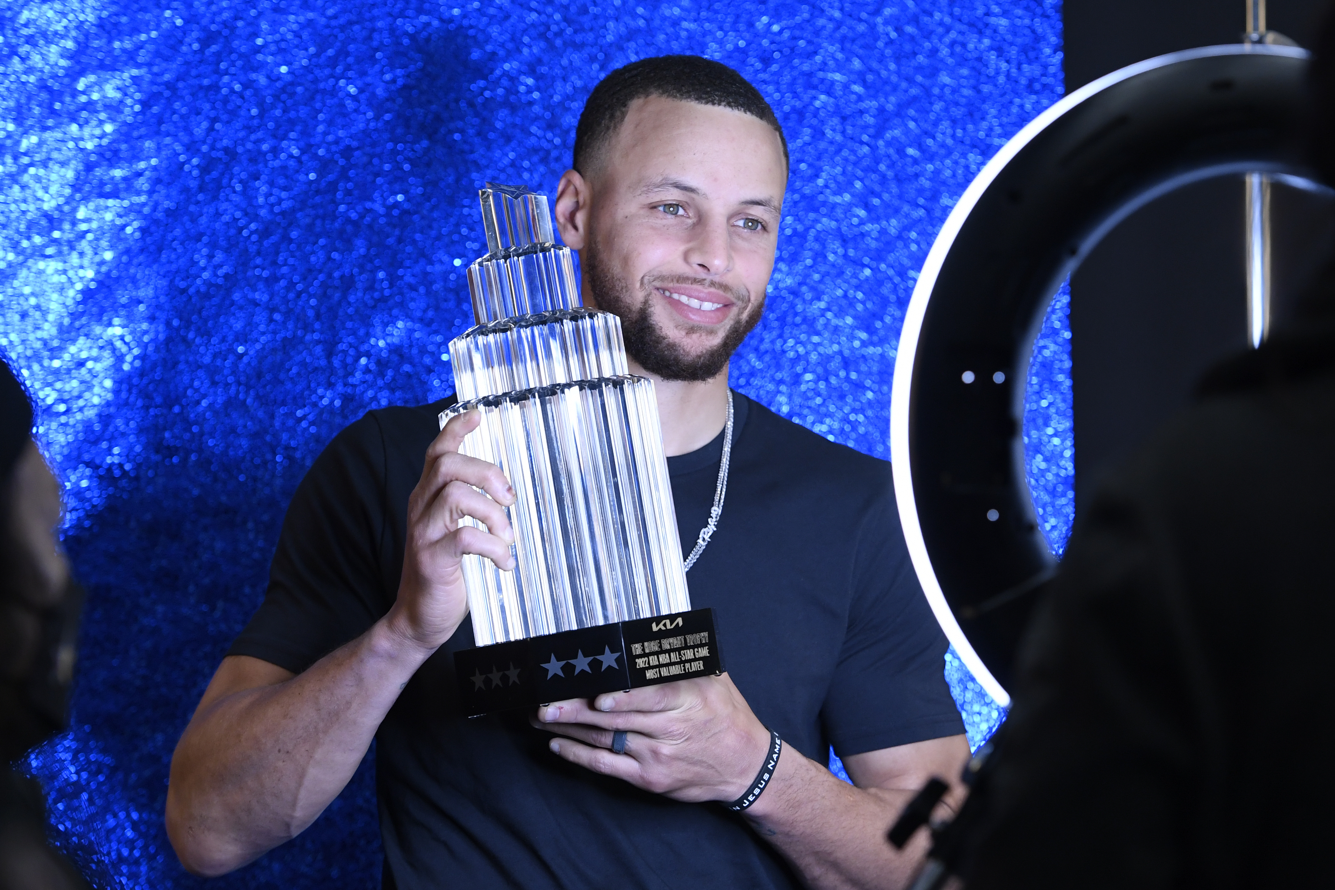 Steph Curry holding up his All-Star GameMVP trophy in front of a ring light