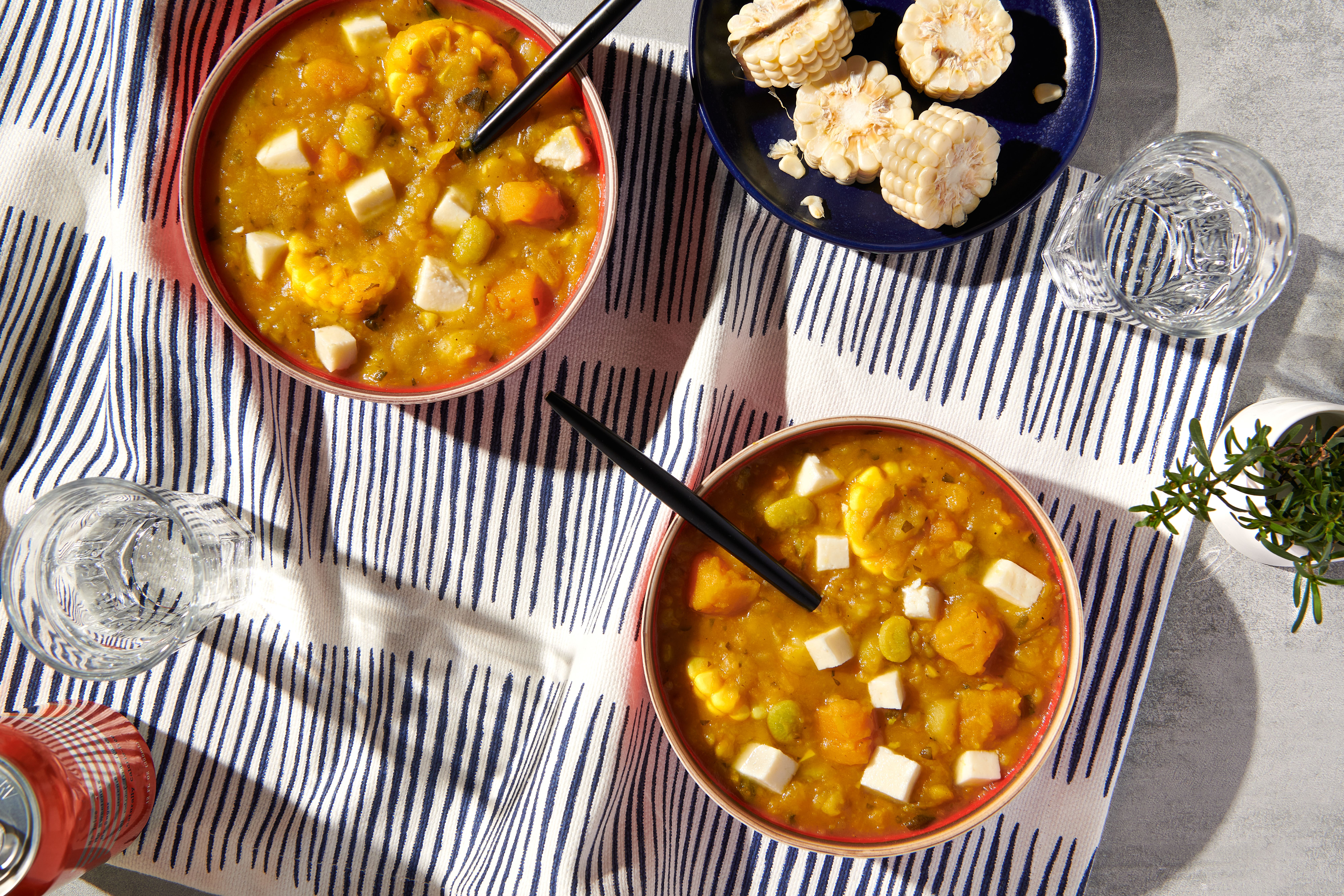 Two bowls of locro on a table, next to another bowl containing sliced corn cobs.