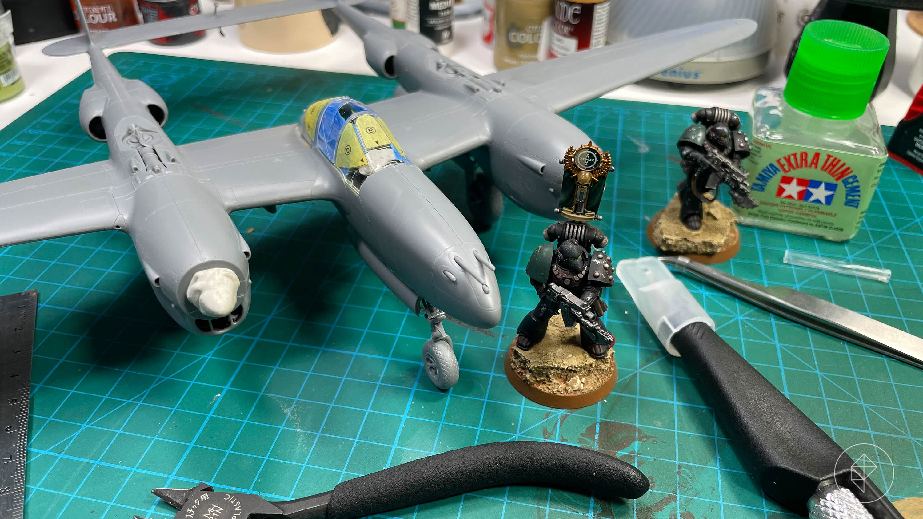 A gray plastic P-38J and a finished space marine on a table with an assortment of hobby tools spread around.