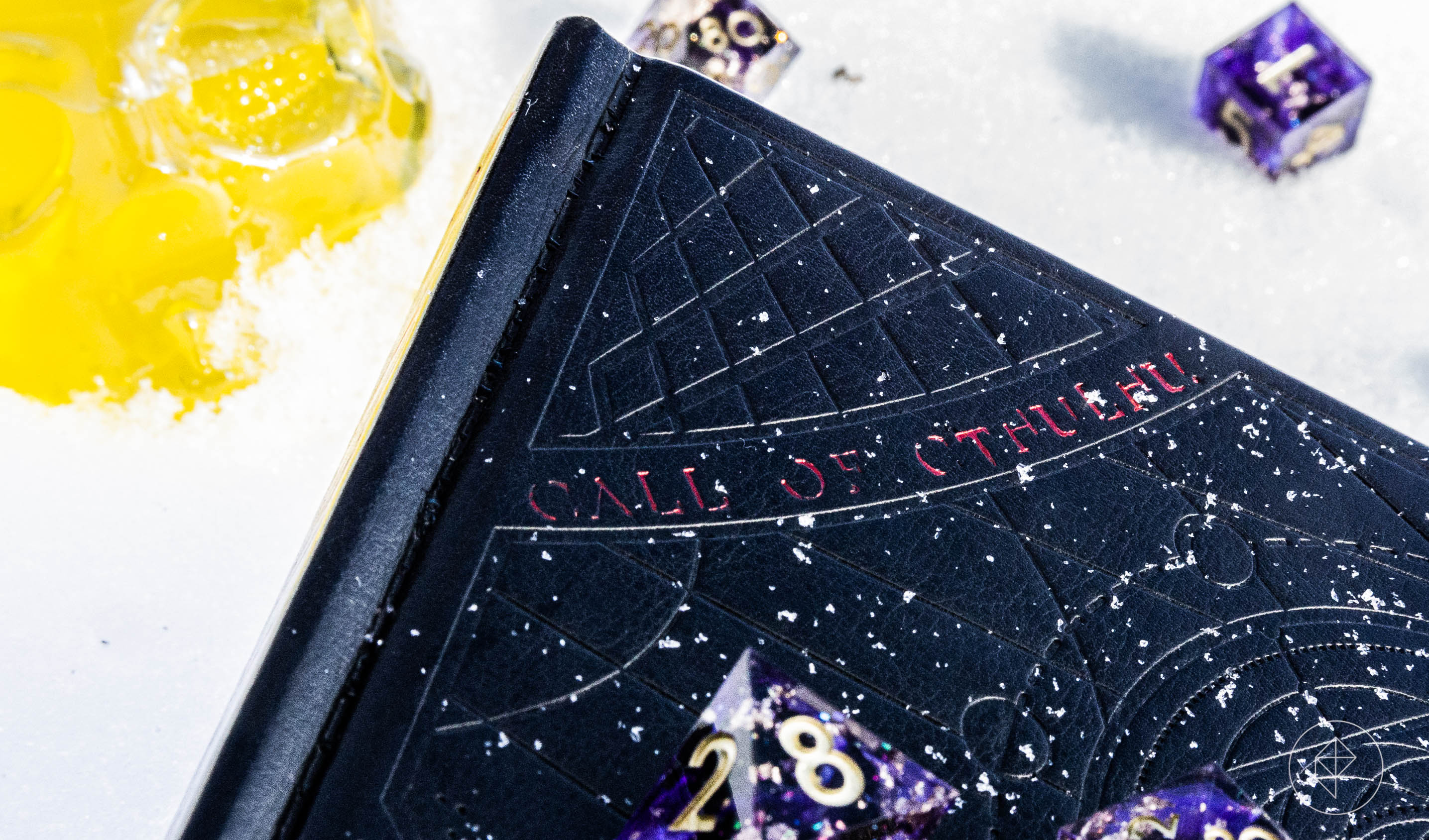 A leather-bound book imprited with arcane sigils sits half buried in the snow. It reads “Call of Cthulhu” in a curving font. A crystal skull and purple dice frame the image.