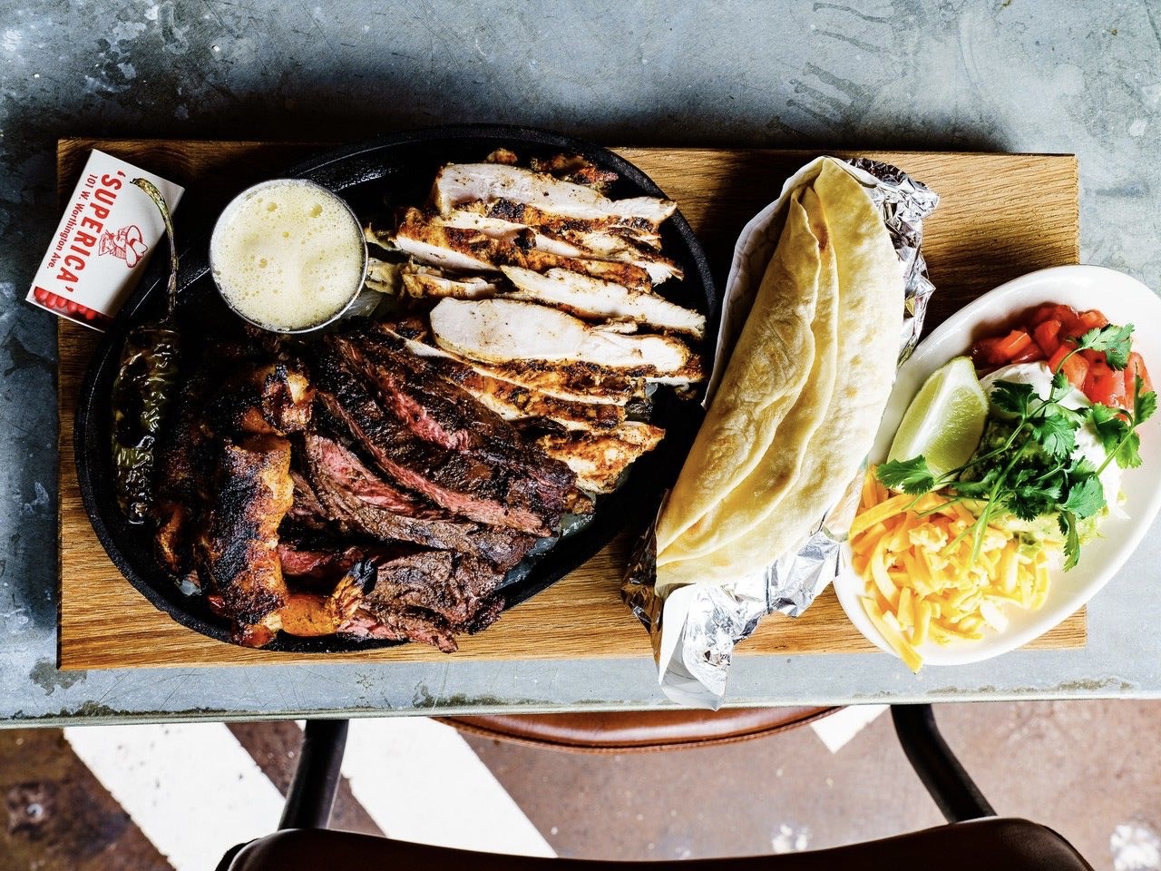 A platter of steak and chicken strips sits beside hot tortillas and a variety of vegetable fixings at Superica. 