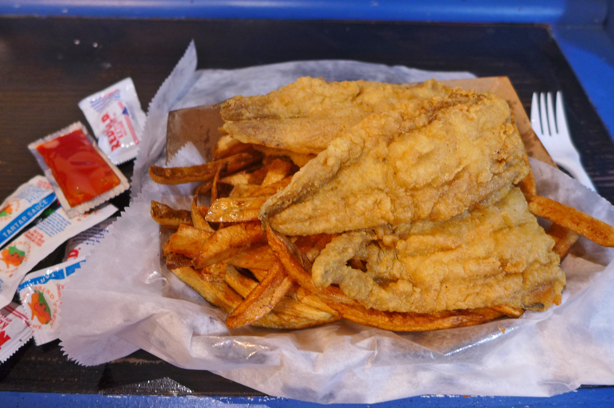 A pile of fried fish filets atop a heap of french fries.
