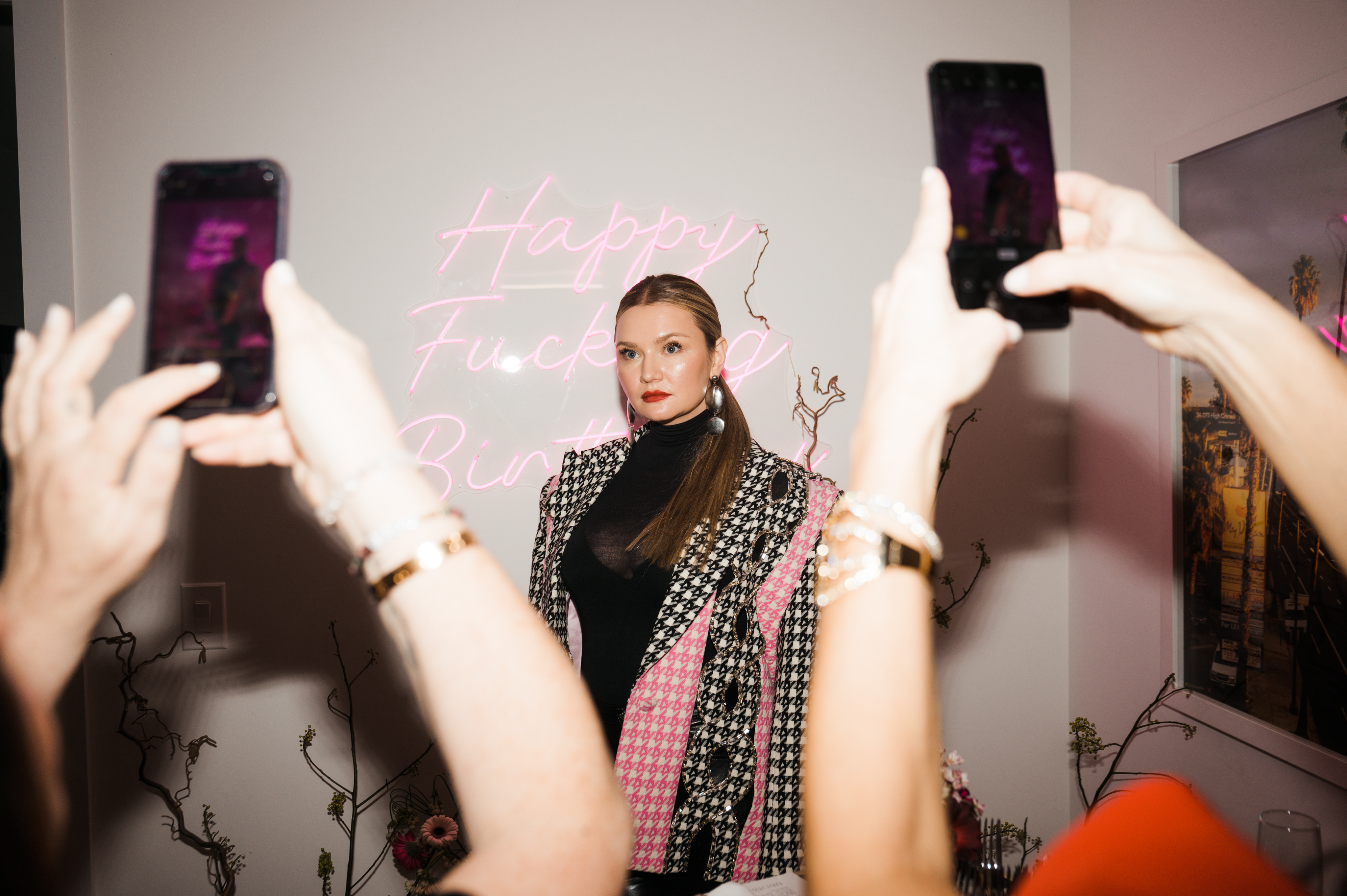 Anna Delvey pictured in her NYC apartment in front of a “Happy Fucking Birthday” neon sign.