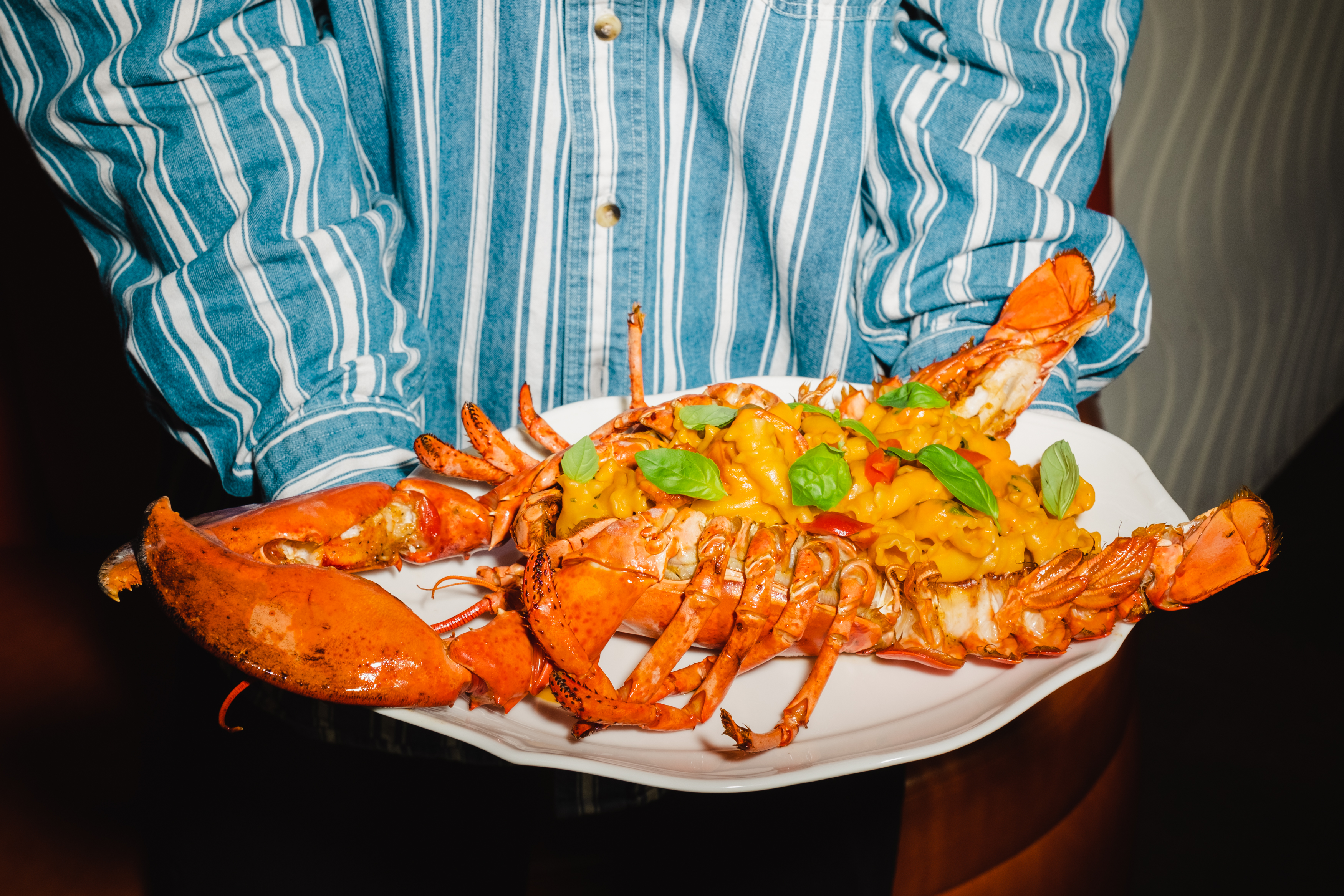 A whole lobster is arranged on a plate with a heap of basil leaves and orange-colored pasta.