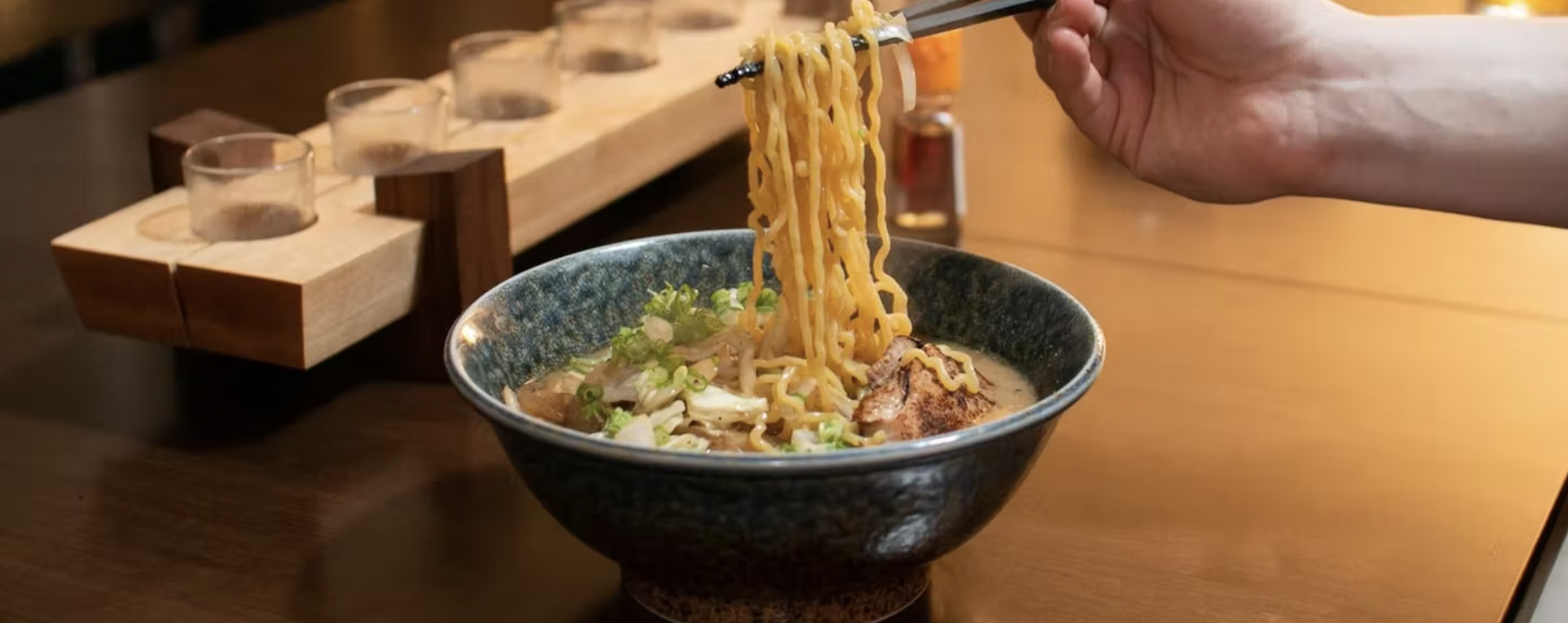 A person uses chopsticks to lift noodles out of a ramen bowl. 
