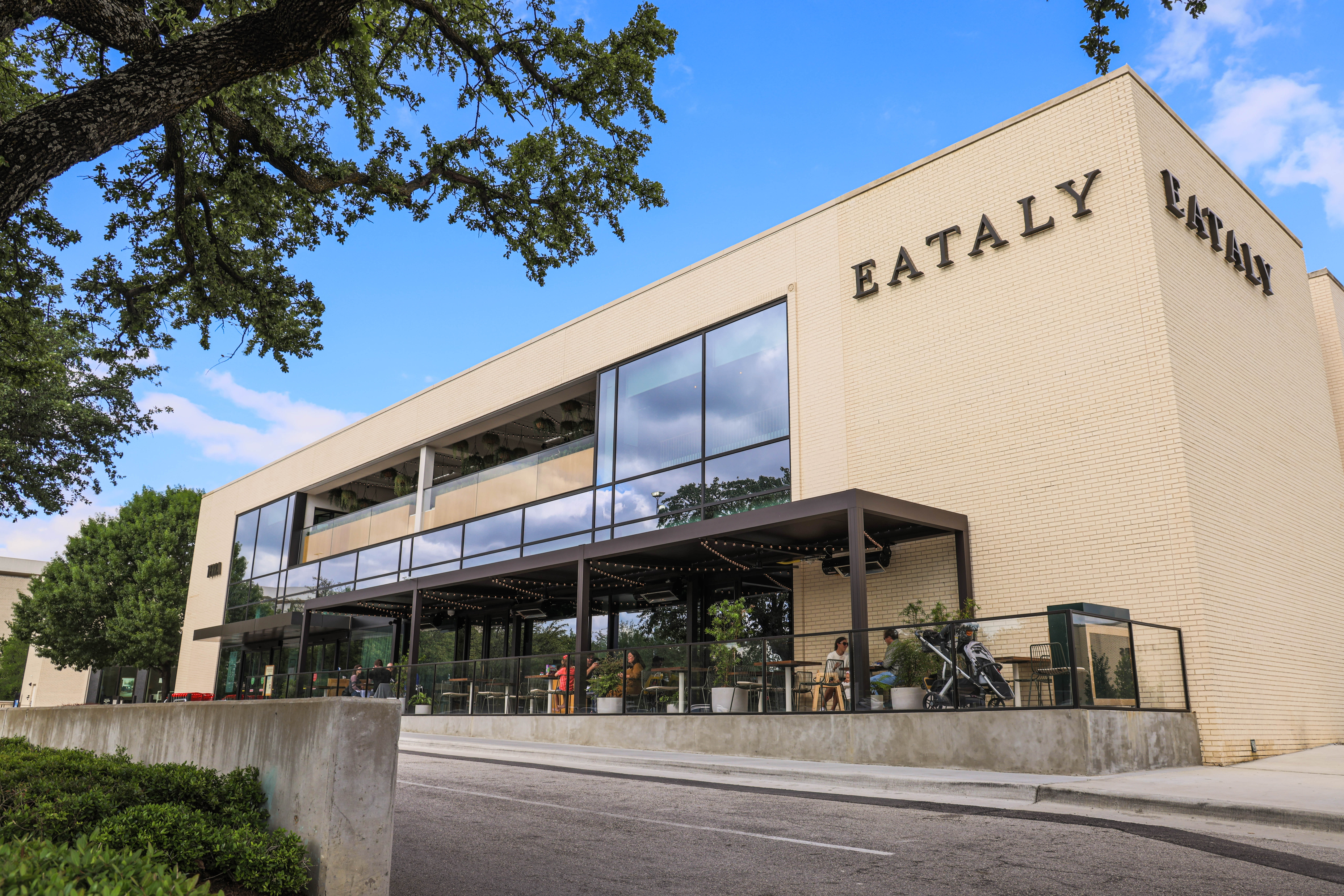 The exterior corner of a large building in cream-colored brick expansive windows and a sign that reads “Eataly.”