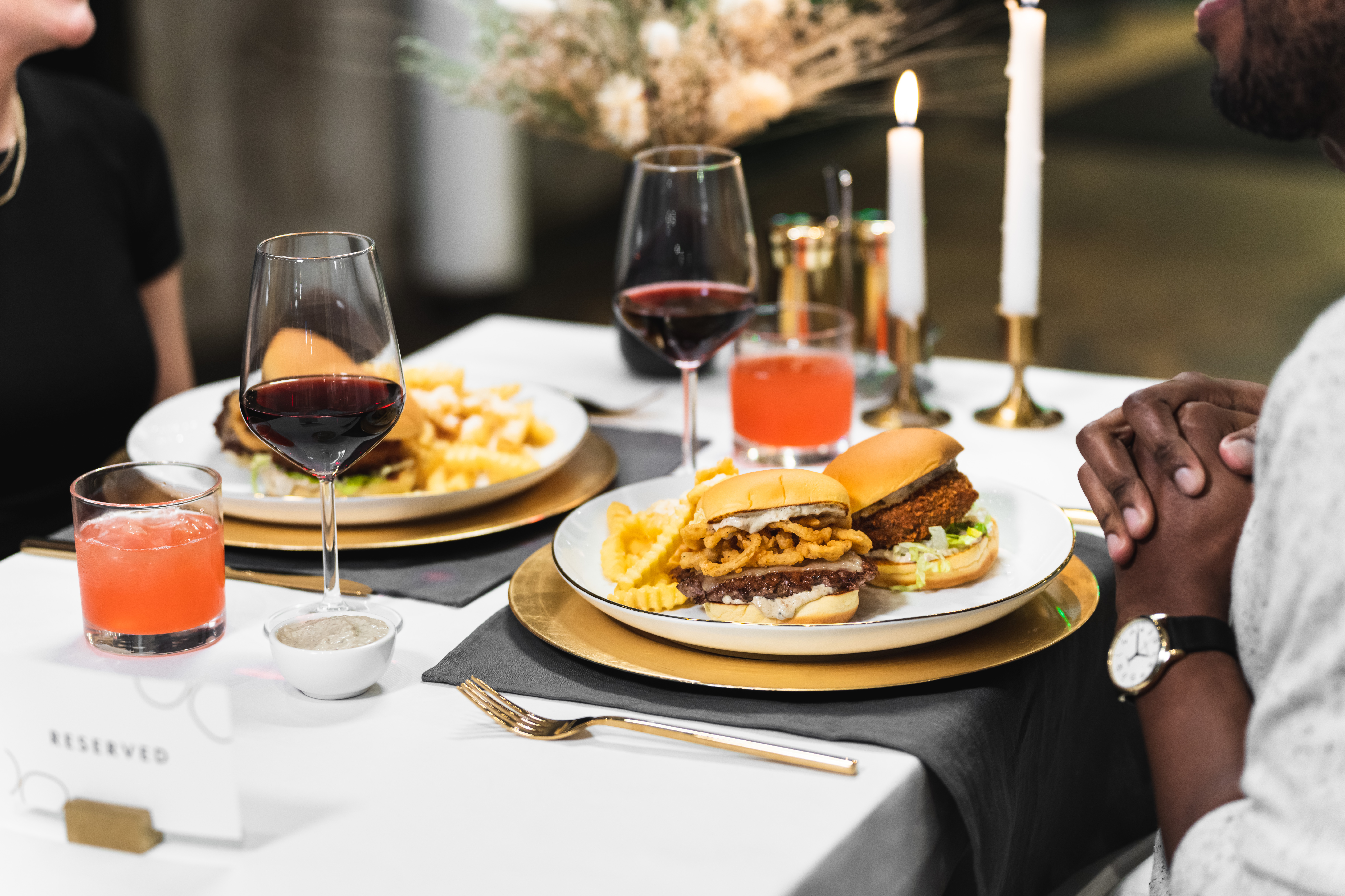 Burgers and crinkle-cut fries are presented on white plates beside golden silverware.