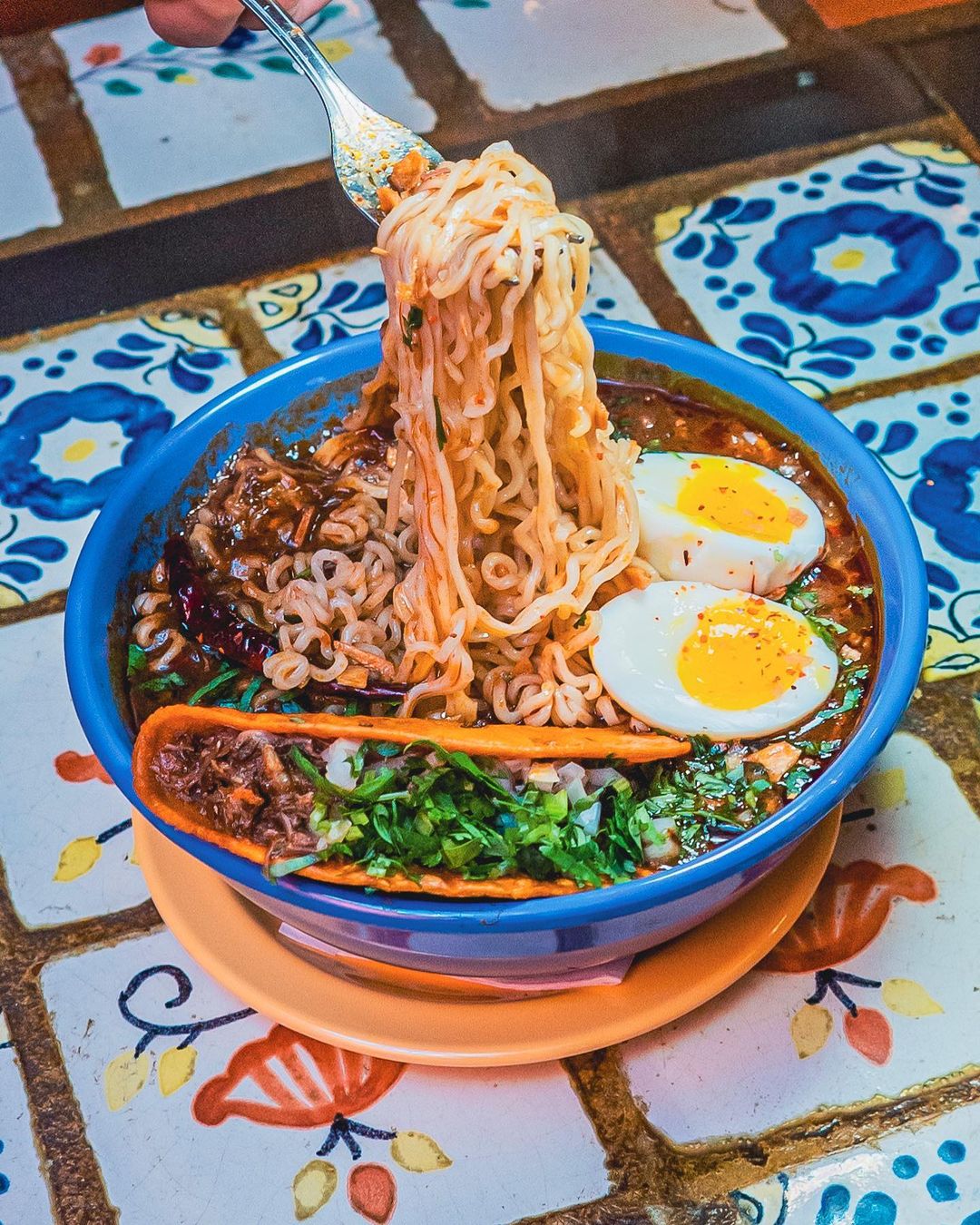 A bowl of birria ramen with a fork pulling noodles from the bowl. 