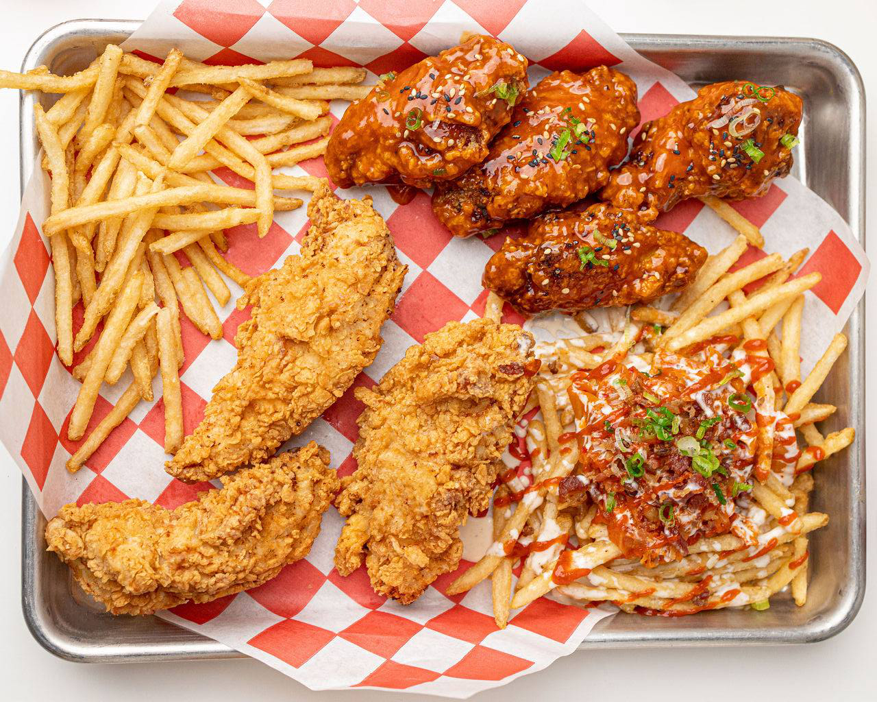 A tray of fried chicken, some dry the other saucy, and fries.