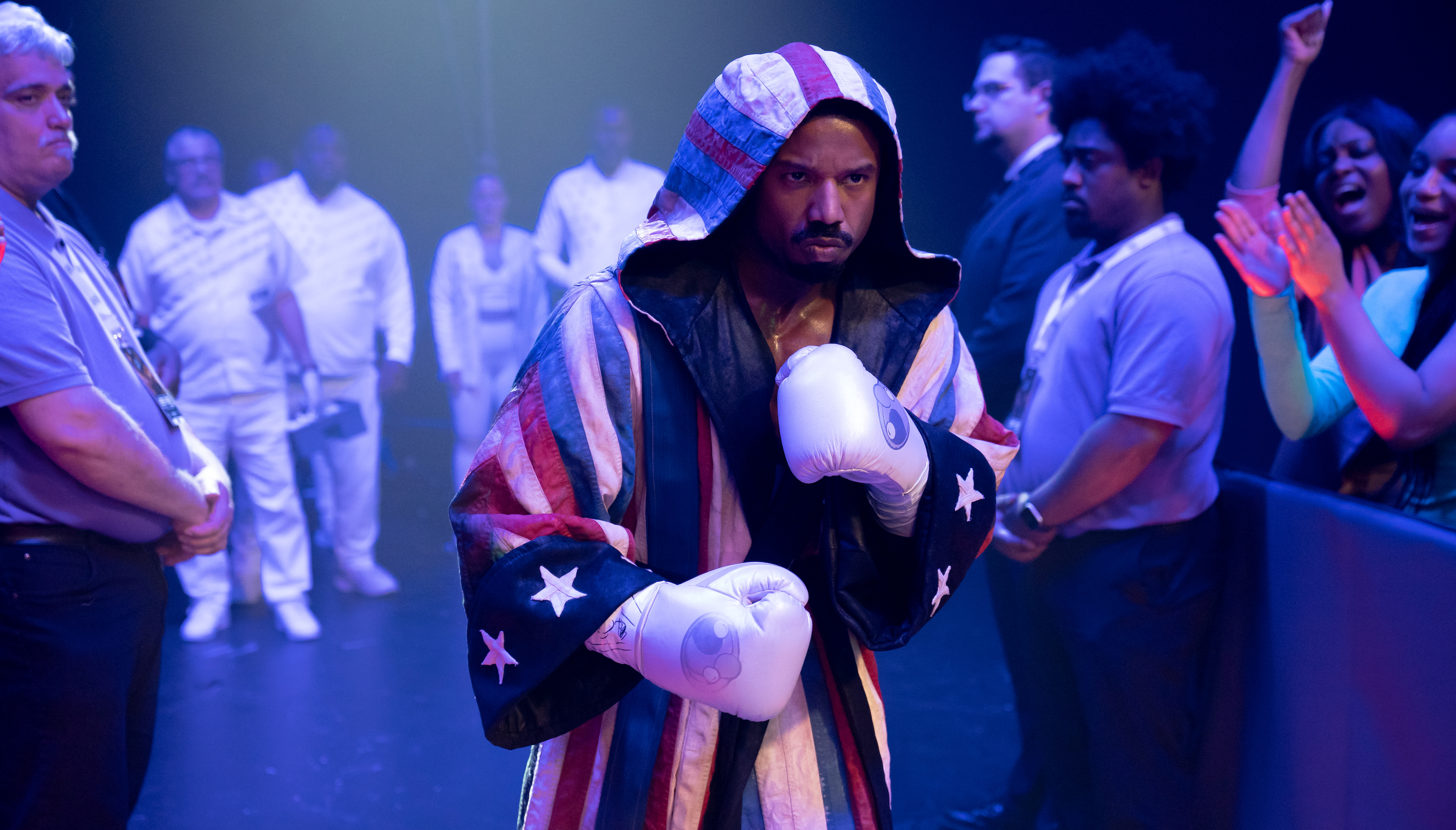 Adonis Creed (Michael B. Jordan) prepares to enter a boxing ring, in white gloves and a red, white, and blue American-flag themed hooded robe in Creed III
