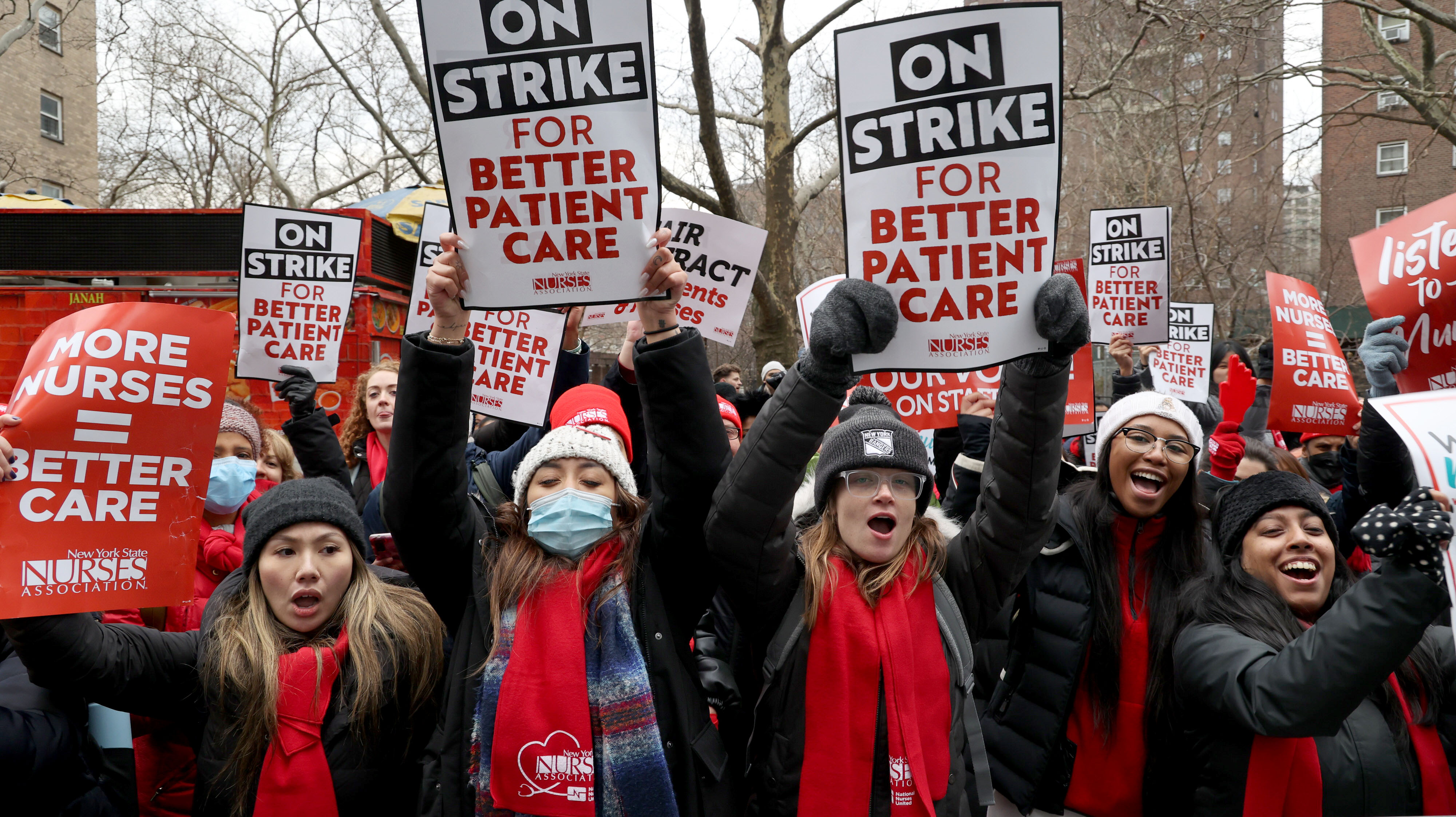 Nurses protesting outside a hospital hold saigns that read, “On strike for better patient care.”