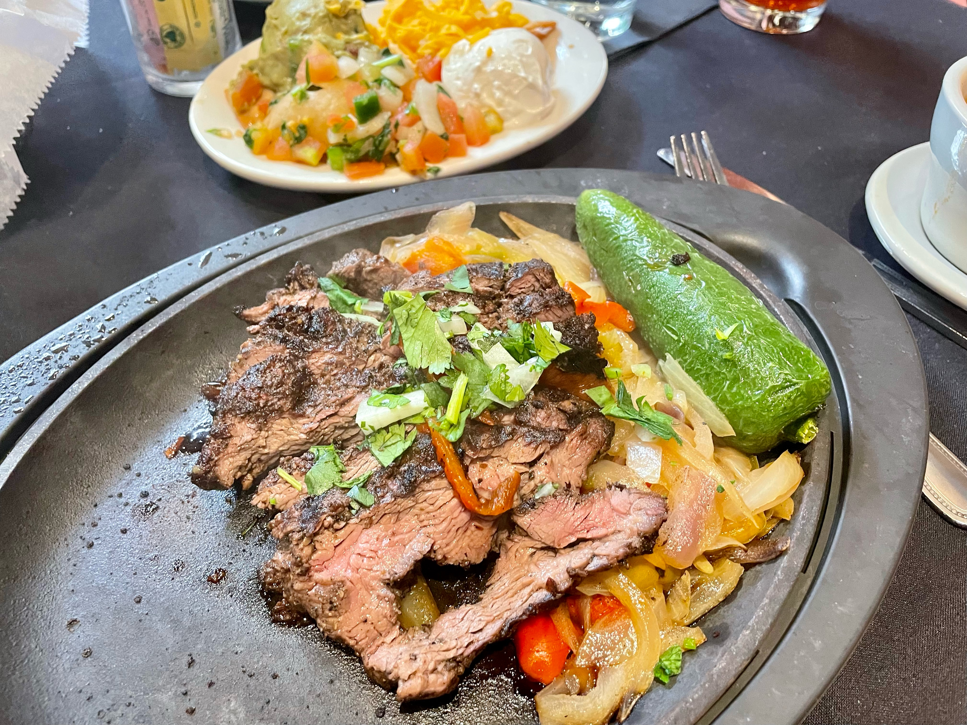 A plate of steak fajitas with onions, bell peppers, and a grilled jalapeno.