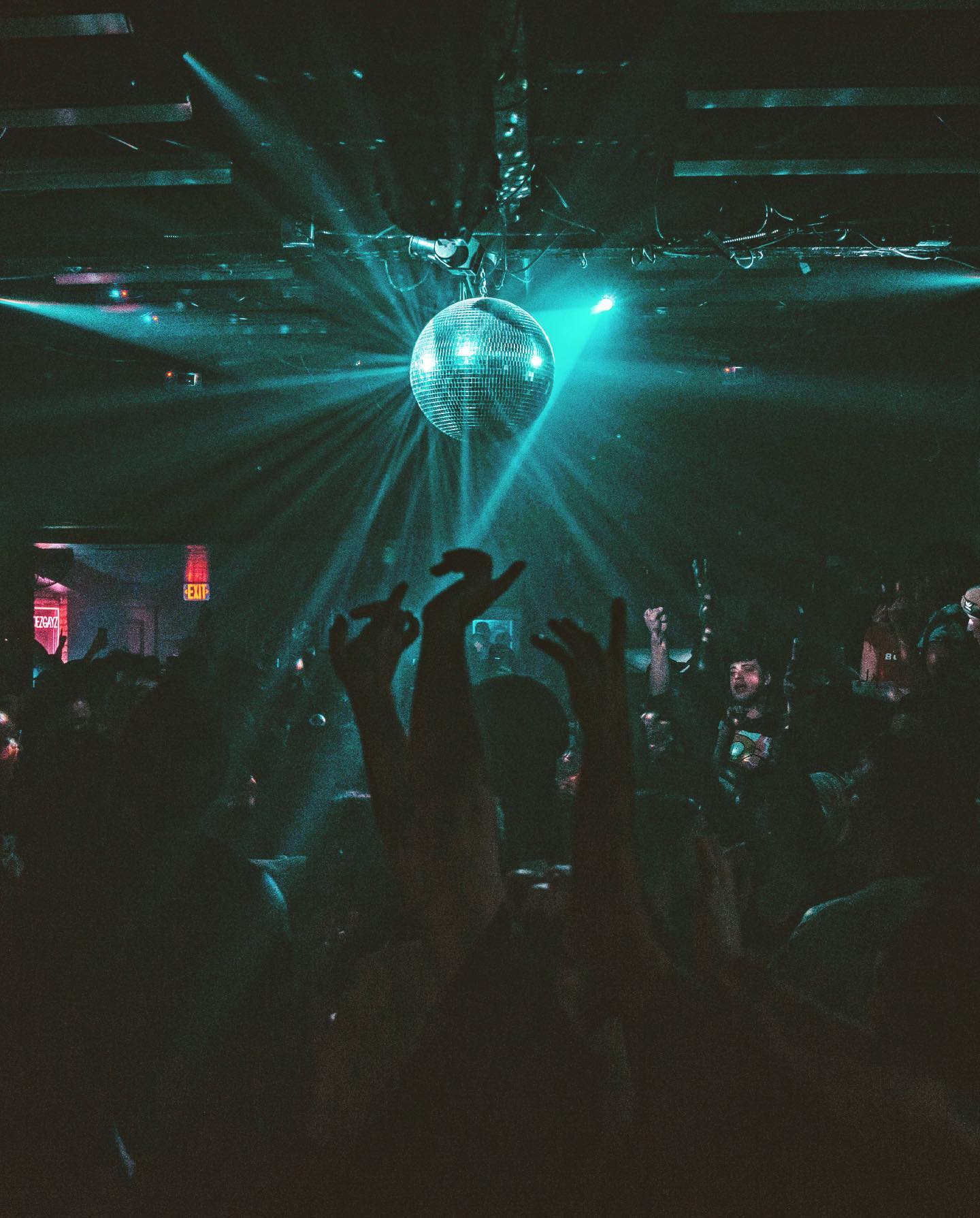 A lit-up disco ball above a dark crowded dance floor.