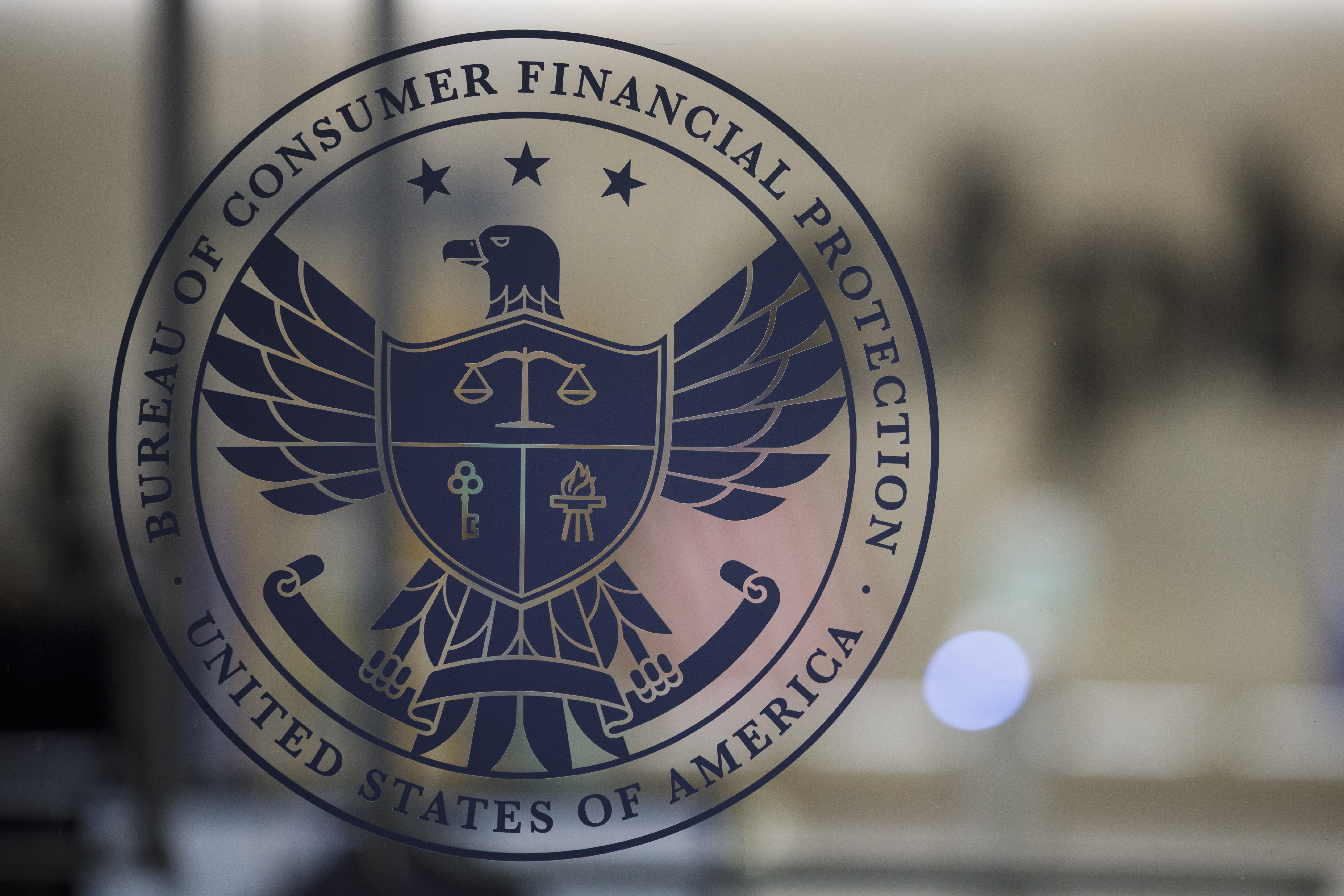 The eagle-shaped logo of the Bureau of Consumer Financial Protection seen on a glass door.