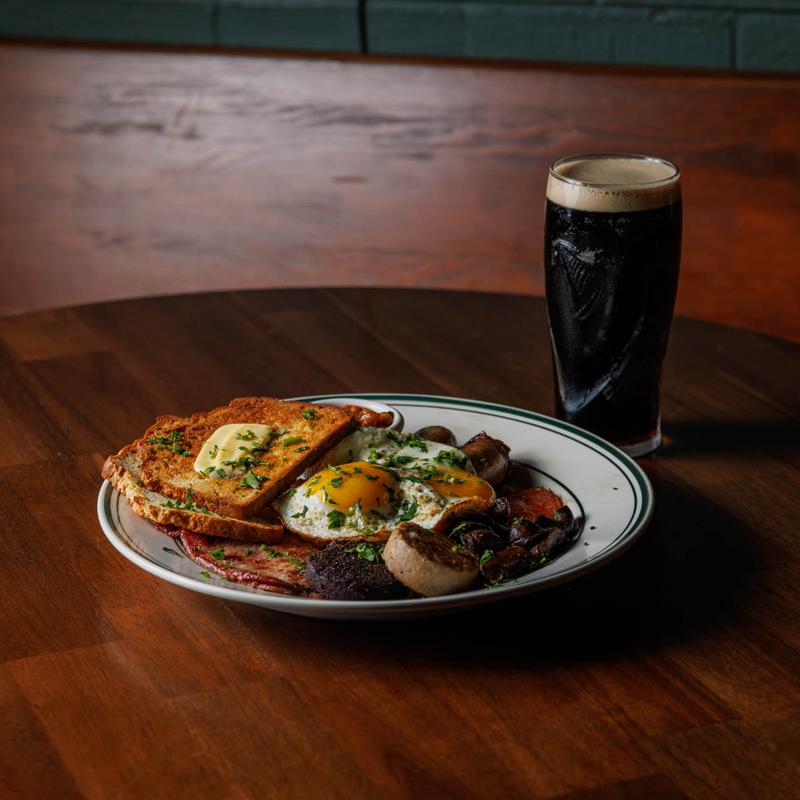 A plate of breakfast next to a glass of dark beer.